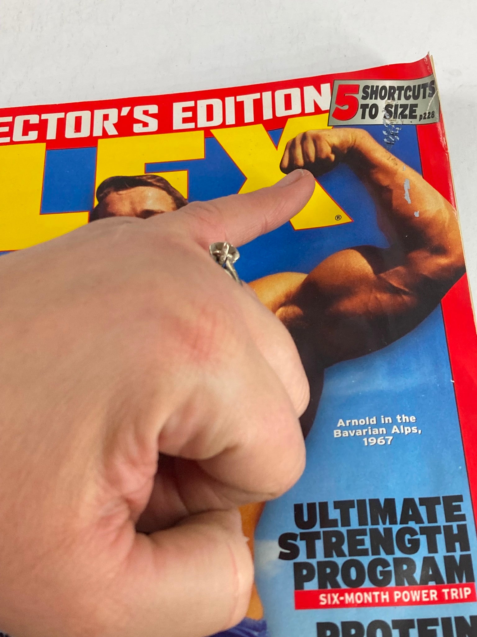 Close-up of the Flex Magazine May 2005 cover pointing to the headline '5 Shortcuts to Size', highlighting Arnold Schwarzenegger, a fitness icon from Volume 23, Issue #3.