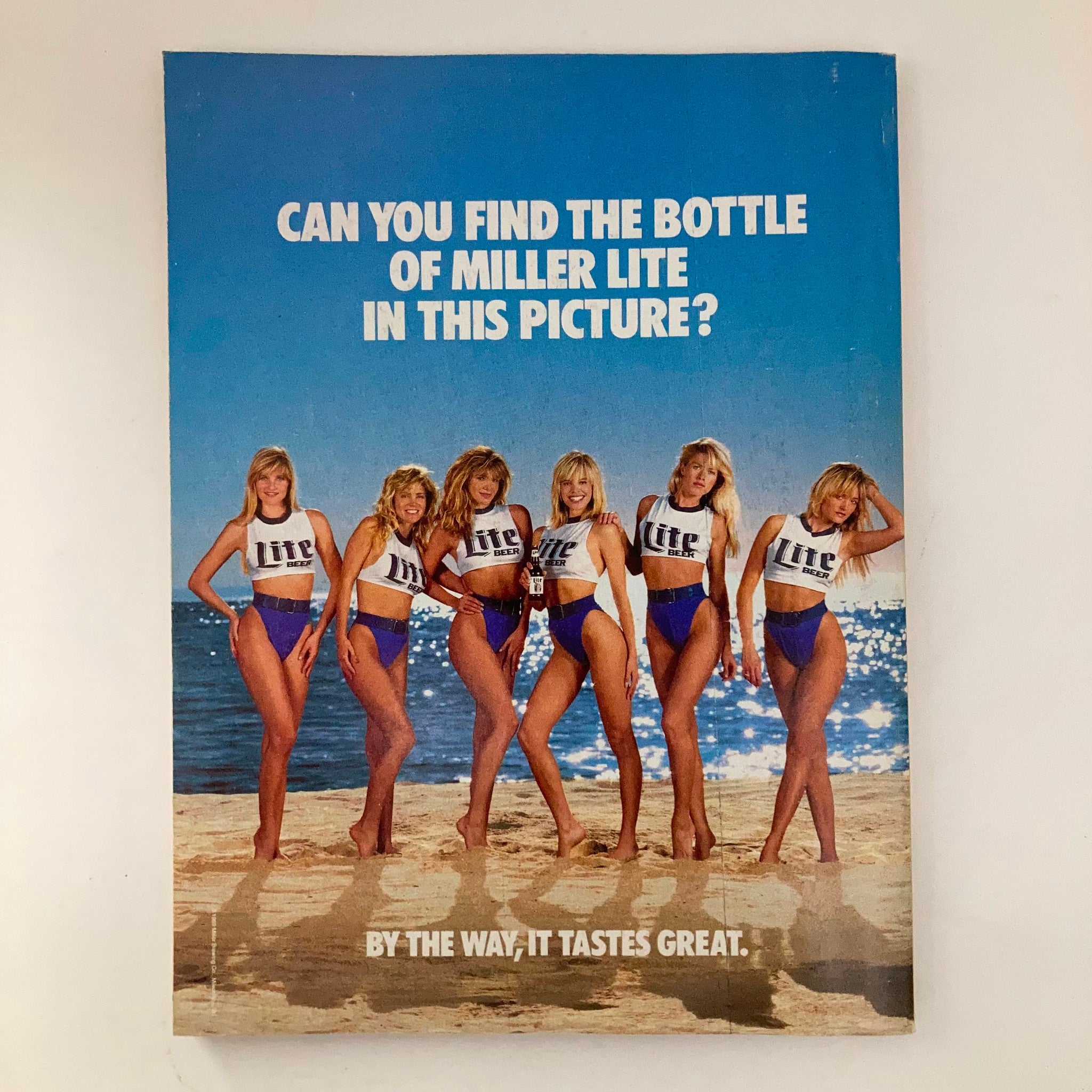 Promotional ad from the May 1989 issue of Joe Weider's Muscle & Fitness Magazine featuring six models in Miller Lite swimwear, posed on the beach with a fun caption about finding the beer bottle.