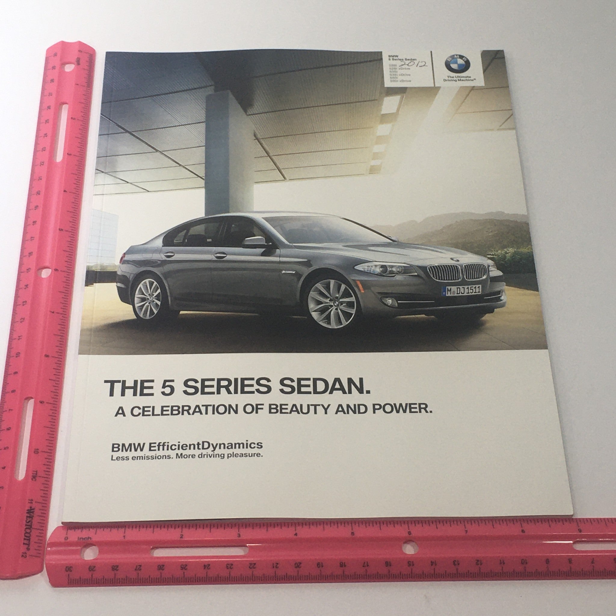 Front view of the 2012 BMW 5 Series Sedan 528i 535i 550i X-D Dealership Car Auto Brochure Catalog showcasing the car with a scenic backdrop.