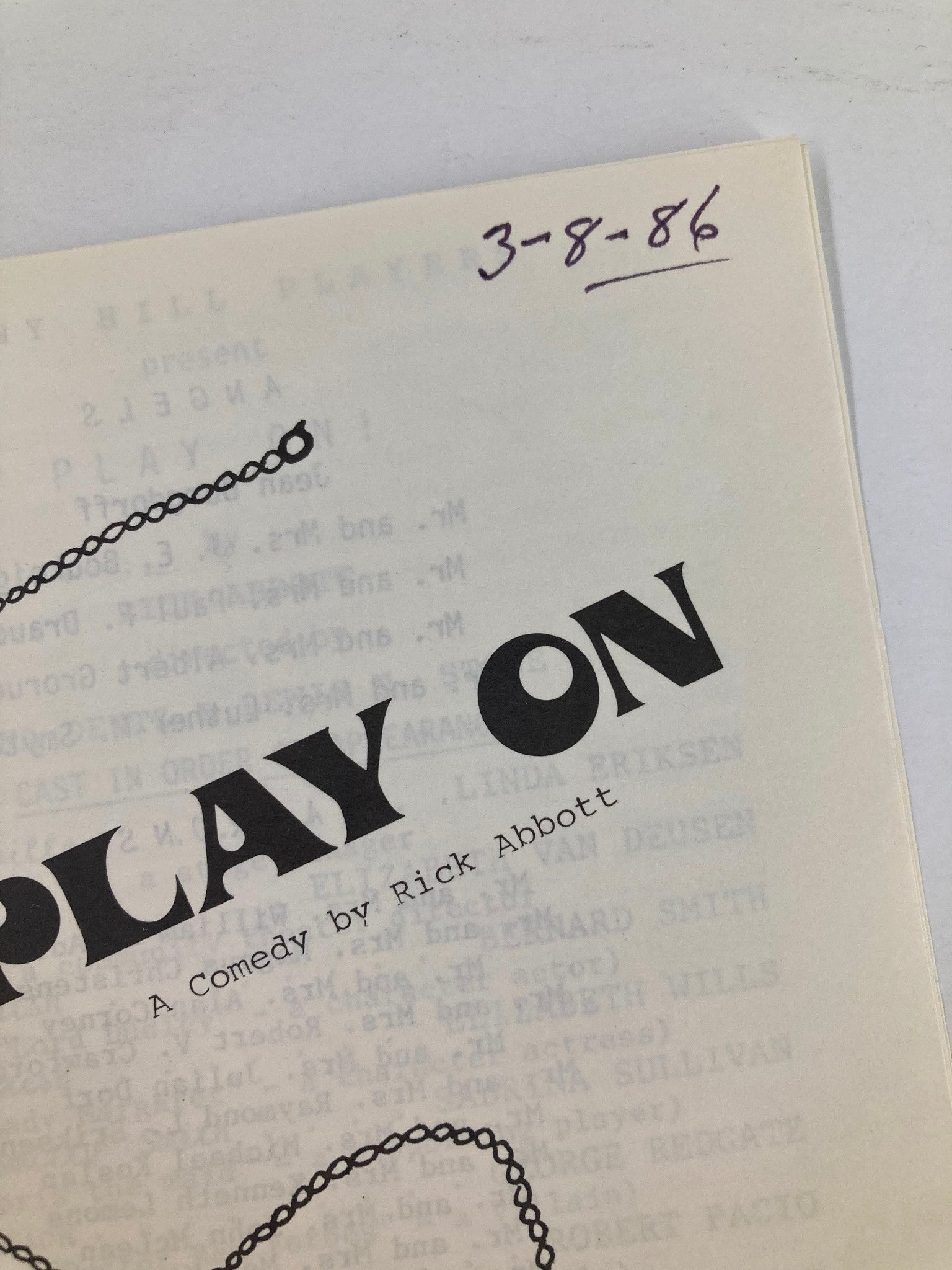Close-up view of the cover of the 1986 Program 'Play On' A Comedy by Rick Abbott, displaying the date 3-8-86 and an intricate pendant design.