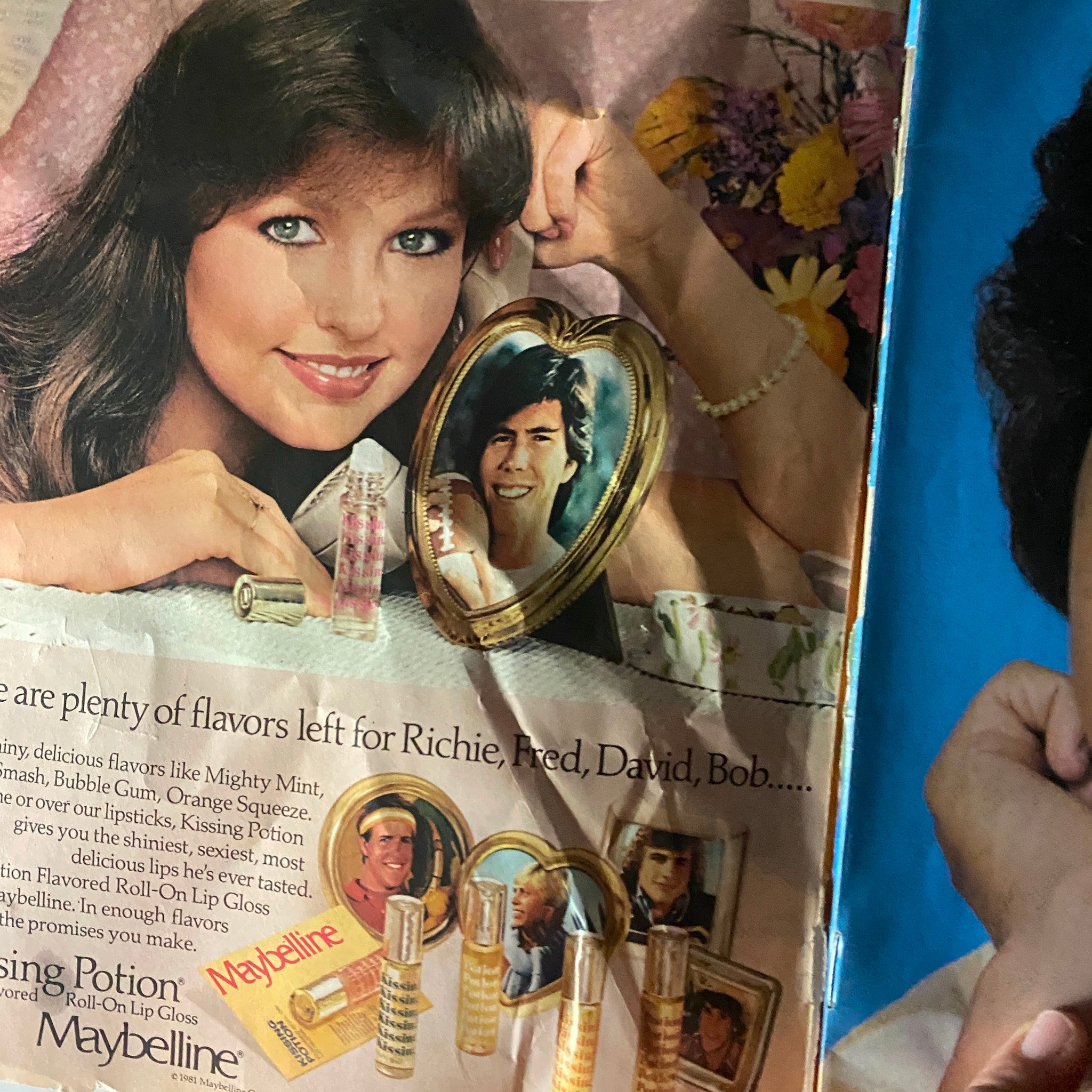 An advertisement featuring a young woman posing with a heart-shaped frame holding a photo of Rick Springfield, promoting Maybelline's Kissing Potion lip gloss.