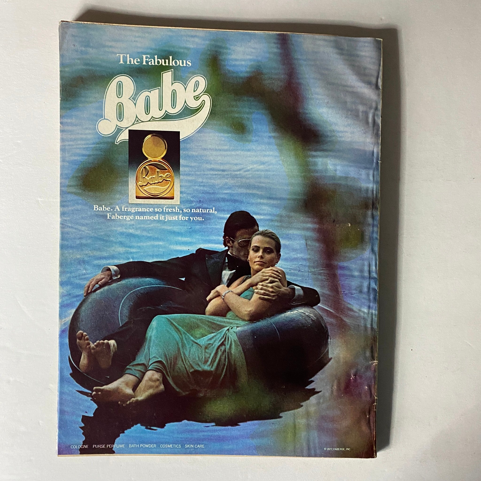 Vintage advertisement from Harper's Bazaar Magazine December 1977 promoting Babe fragrance, featuring a serene image of a couple lounging together.