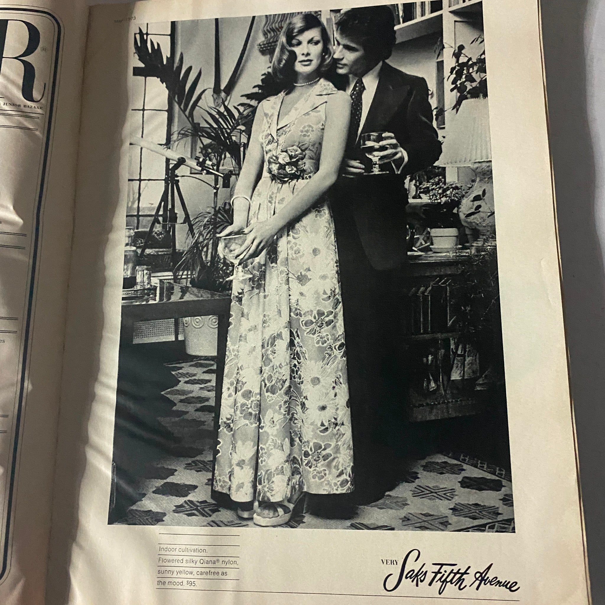 Vintage black and white advertisement featuring a model in a floral gown from the Harper's Bazaar Magazine, May 1973, showcasing early 1970s fashion elegance.