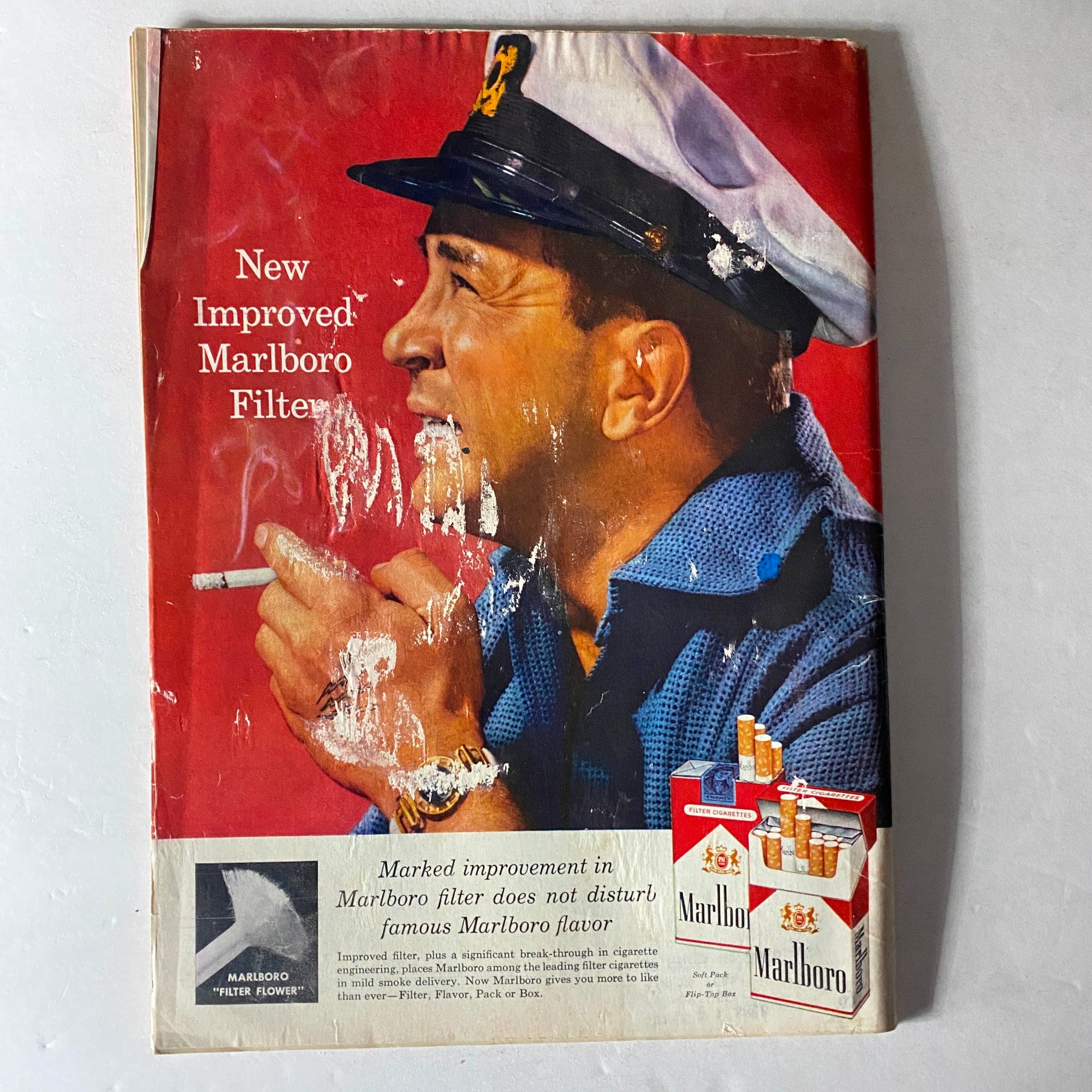 Back cover of a vintage magazine advertising the New Improved Marlboro Filter, depicting a man in a sailor's cap enjoying a cigarette, reflecting mid-20th century American advertising trends.