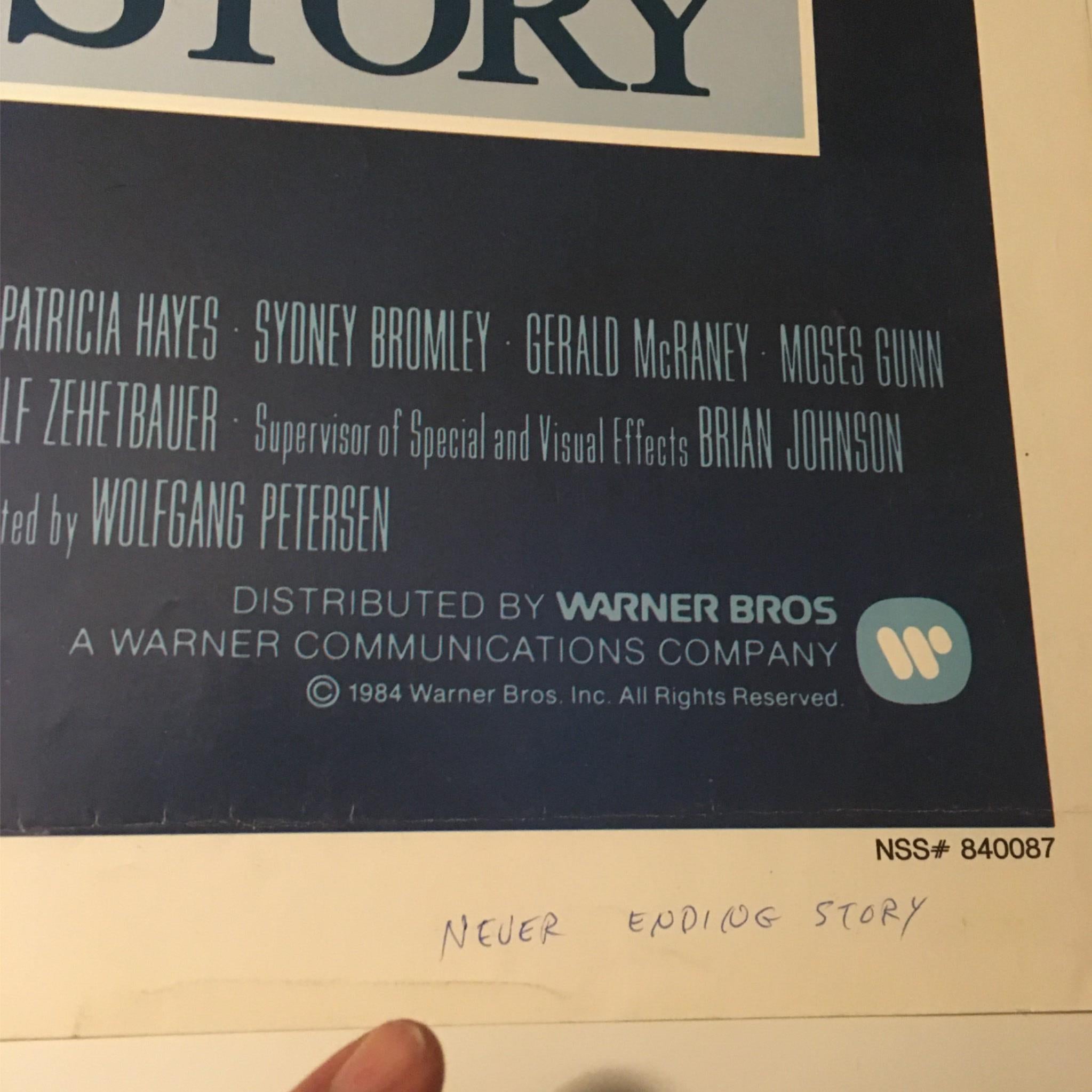 Close-up of the credits from the 1984 film The Never Ending Story movie poster, showcasing the names of key contributors including Wolfgang Petersen. Featuring details about distribution by Warner Bros.