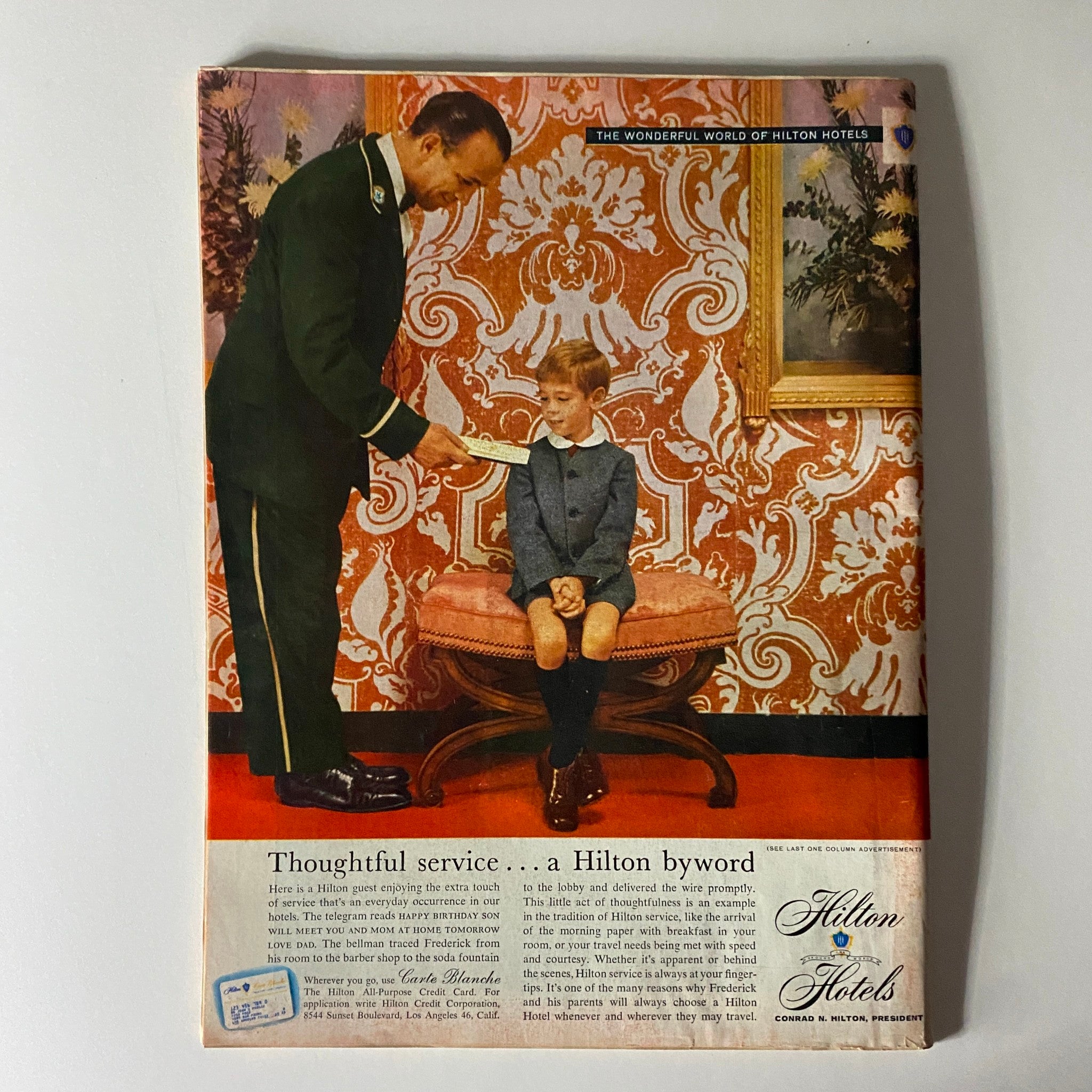 Rear cover of a vintage magazine showcasing a Hilton Hotels advertisement, depicting a bellman assisting a child in a luxurious setting, emphasizing quality service and hospitality.