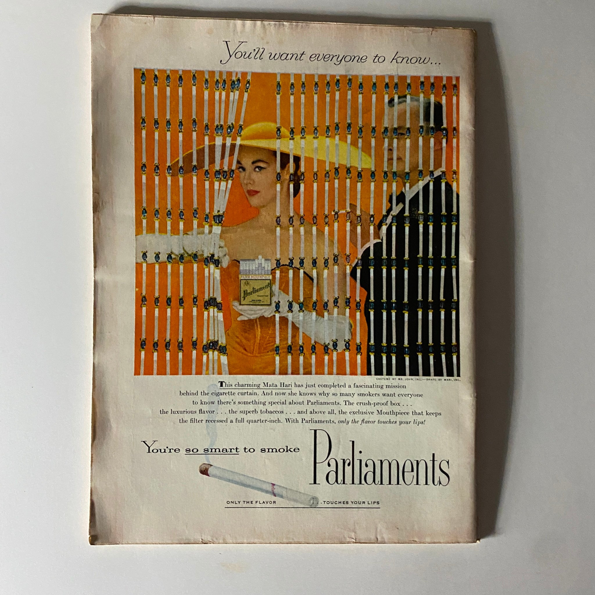 Vintage advertisement from a magazine page, featuring an elegant woman in a yellow hat and a man in a suit, promoting Parliaments cigarettes, with a unique artistic design.