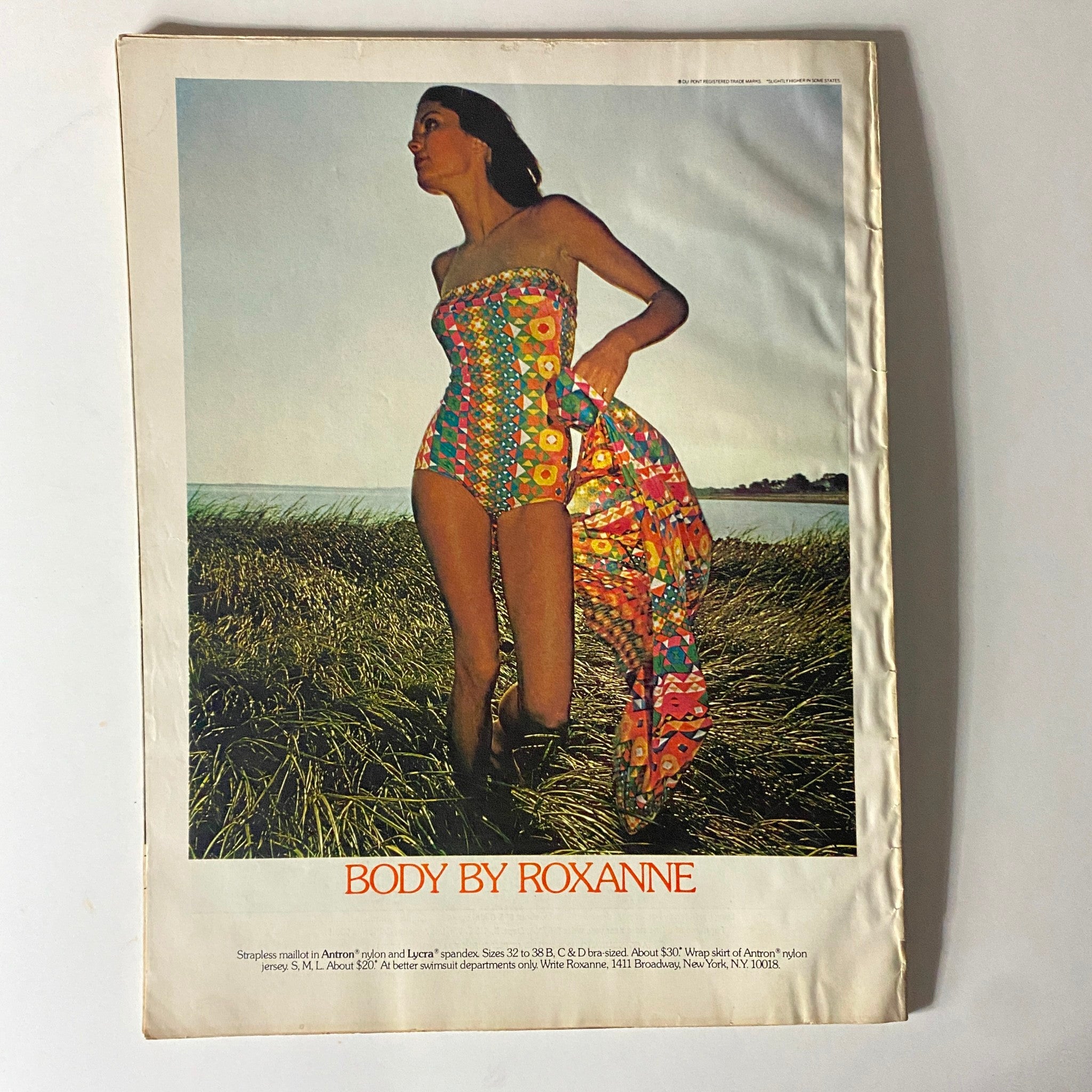 Fashion advertisement from Harper's Bazaar Magazine January 1974 featuring a model in a colorful vintage swimsuit, titled 'Body by Roxanne.' The model stands in a grassy area with a scenic background, embodying the vibrant fashion trends of the early 1970s.