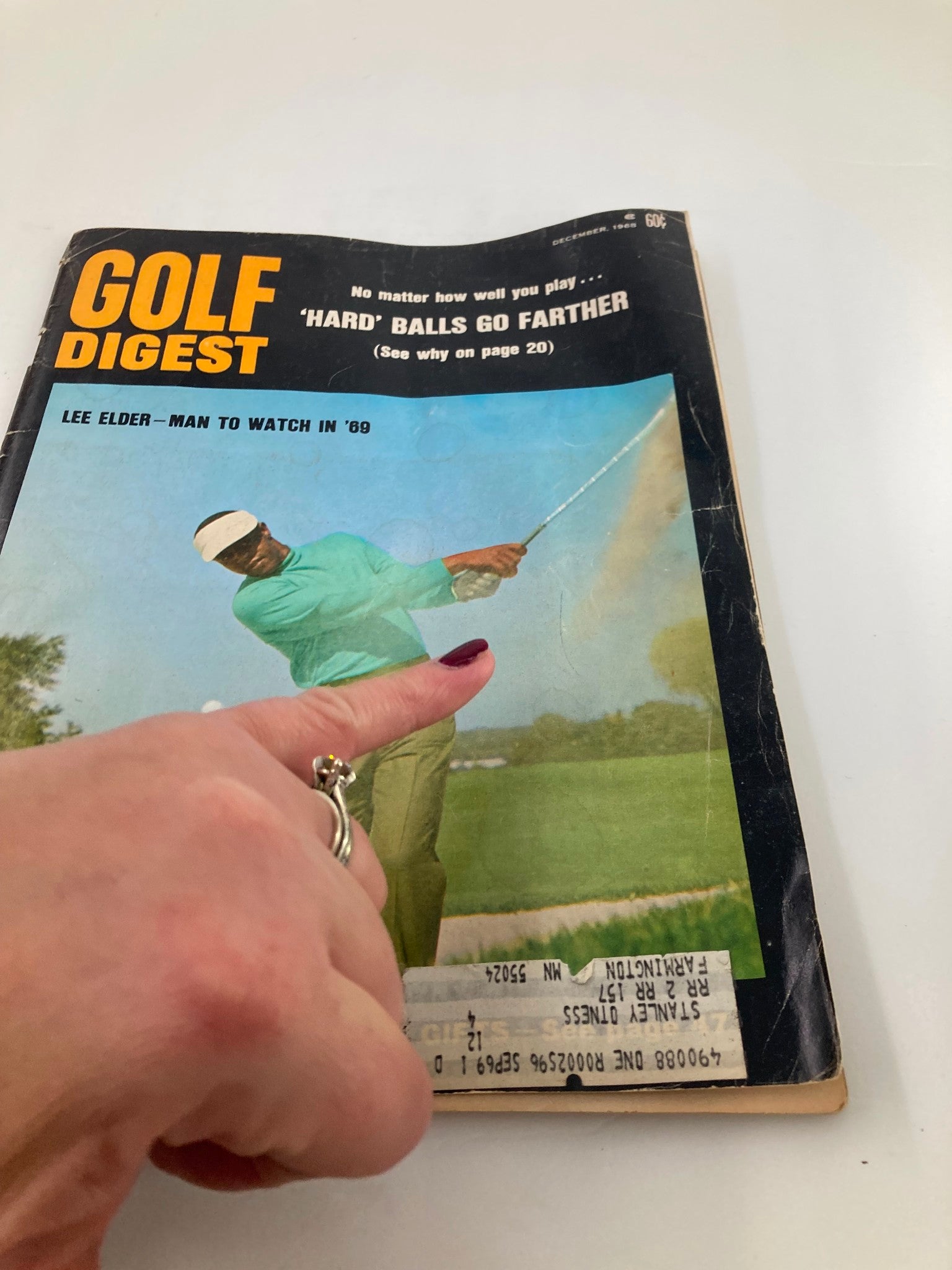 Close-up view of the VTG Golf Digest Magazine December 1968 highlighting Lee Elder as 'Man to Watch in 69', with a hand pointing at the magazine cover.