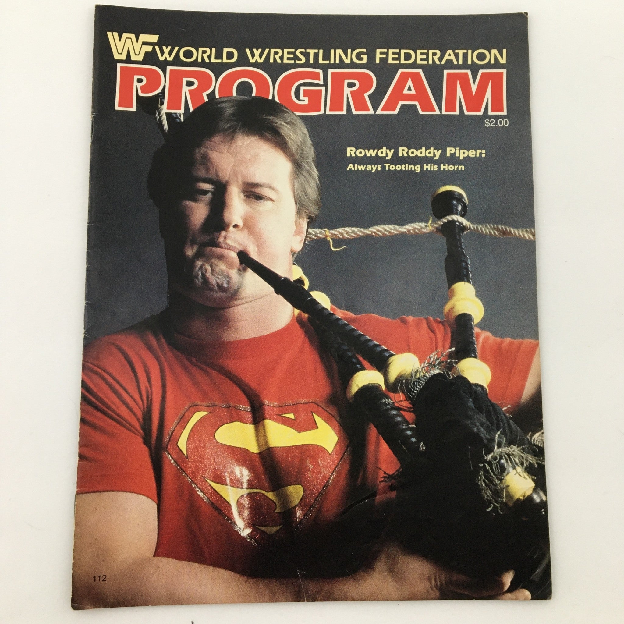 WWF Program 1984 featuring Rowdy Roddy Piper on the cover, showcasing him in a superhero-themed shirt while playing bagpipes.