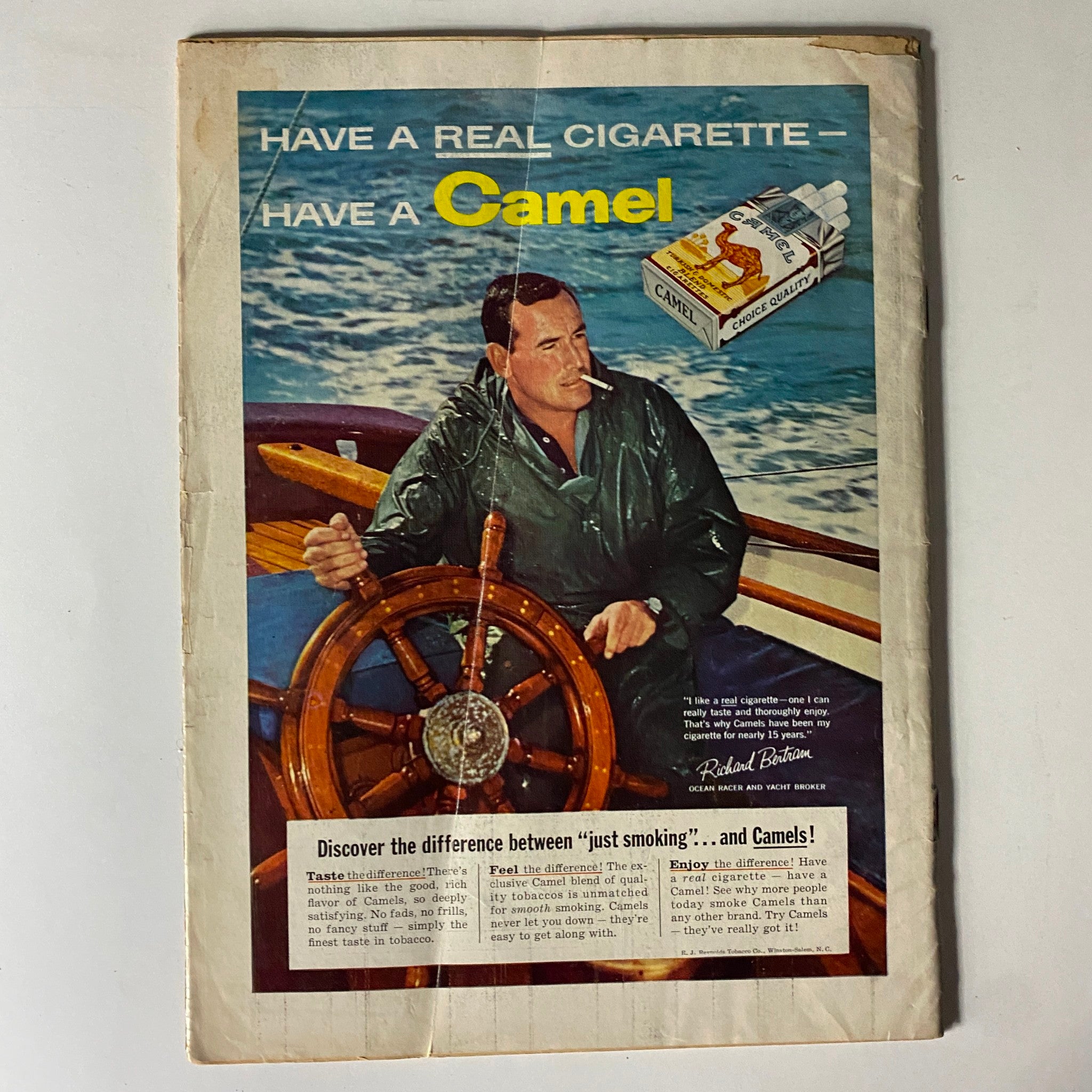 Advertisement from the back cover of The American Legion Magazine August 1957 featuring a man at the helm of a boat promoting Camel cigarettes.