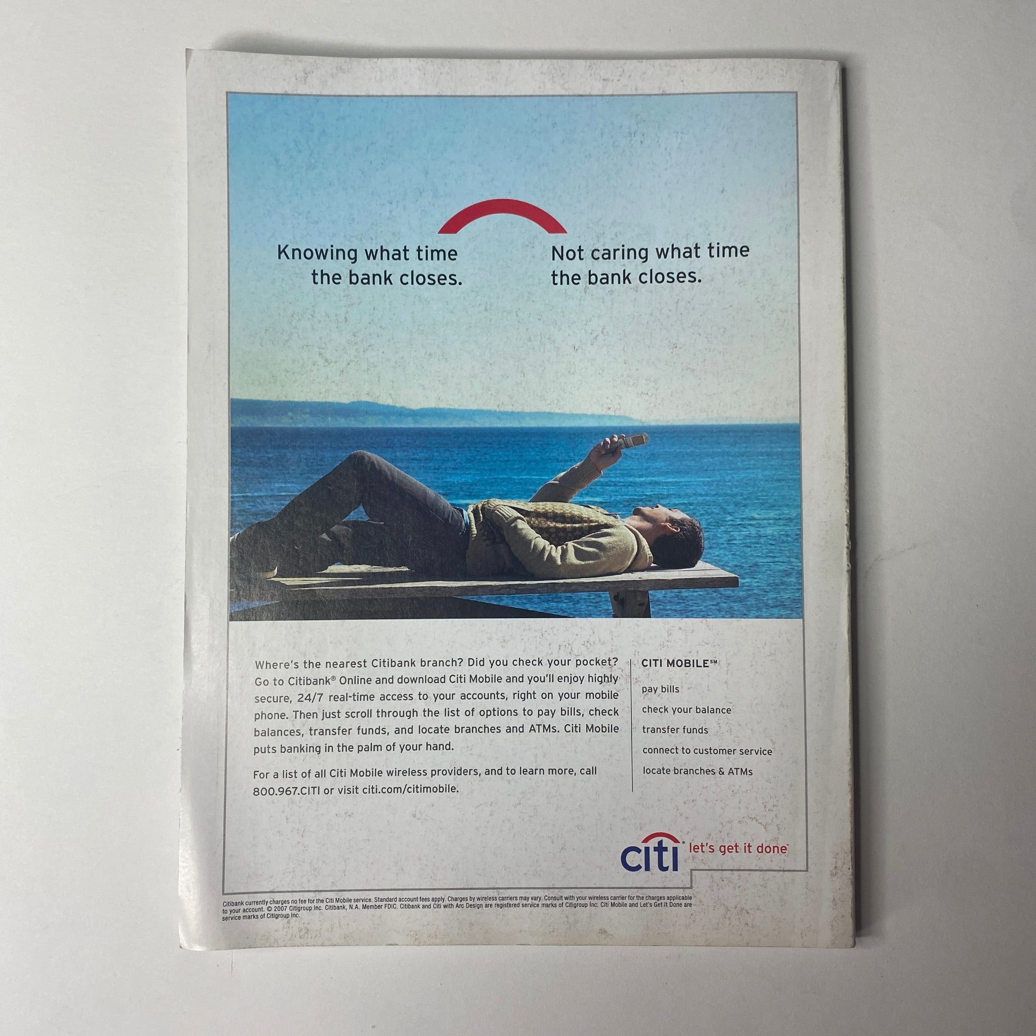 Back cover of Vogue Magazine July 2007 featuring a relaxed scene of a man lying on a beach while using a mobile device, emphasizing the convenience of modern banking, with a tagline related to banking hours.
