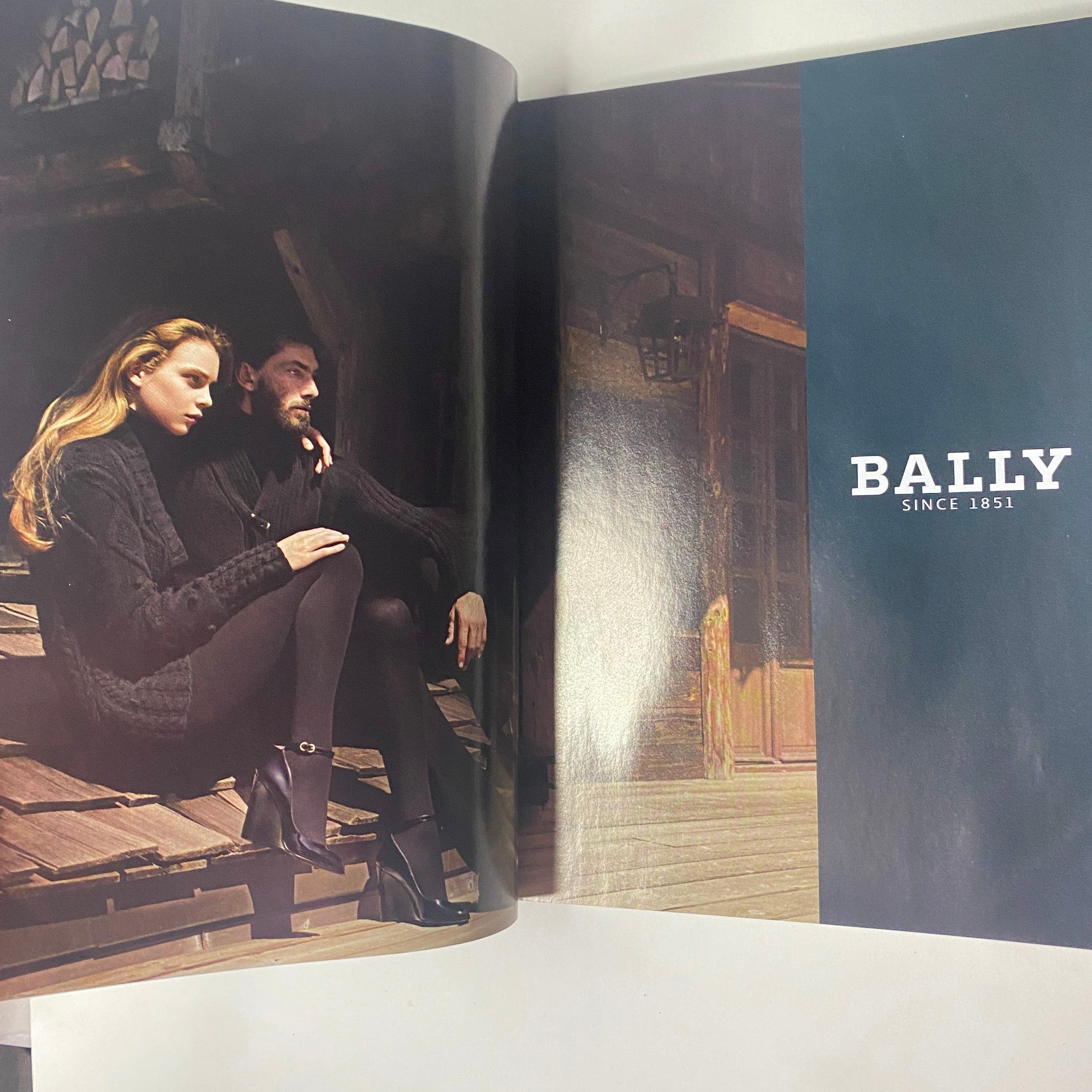 Bally advertisement featuring a stylish model seated on a rustic porch, highlighted in Vogue Magazine August 2007 with Winona Ryder on the cover. Emphasizing modern fashion and elegance.