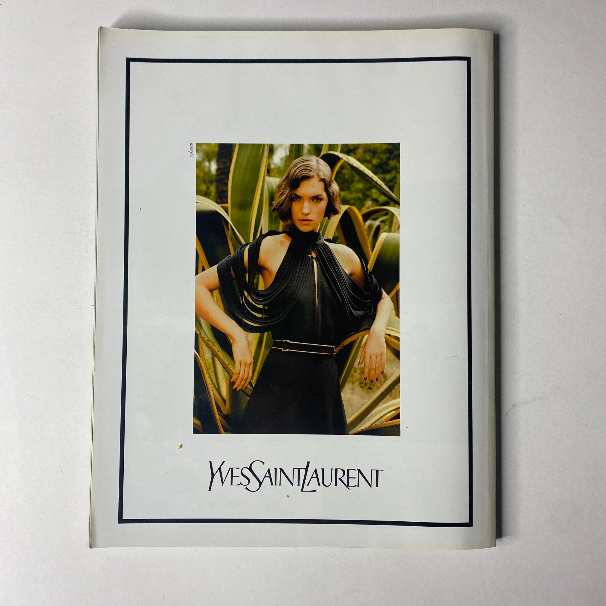 Wes Saint Laurent advertisement displaying a model in an elegant black dress, set against a natural background, from the Vogue Paris Magazine April 2011 No. 916 Gisele Bündchen Cover.