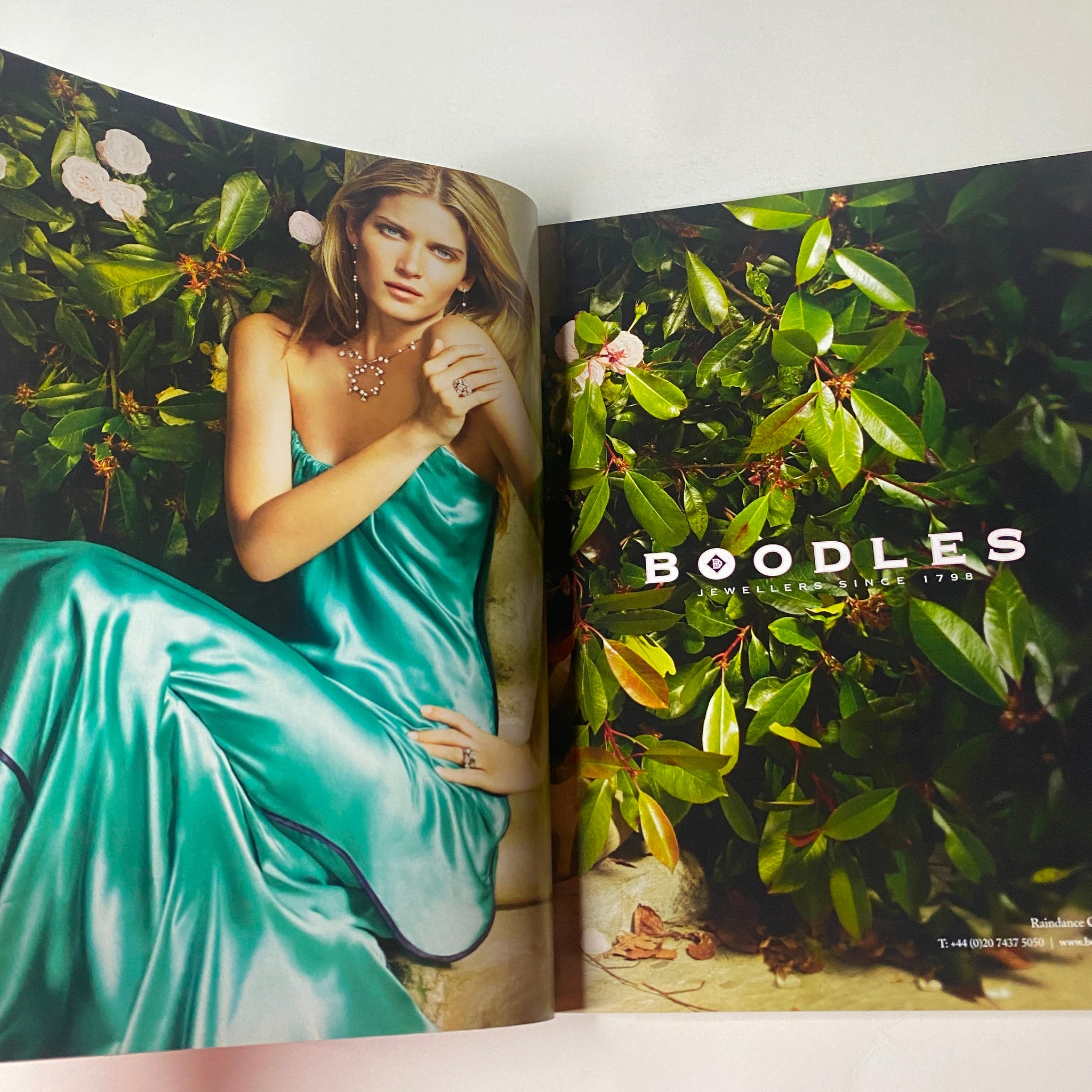 Boodles jewelry advertisement from Vogue British Magazine July 2010 featuring a model in a teal satin dress amidst lush greenery.