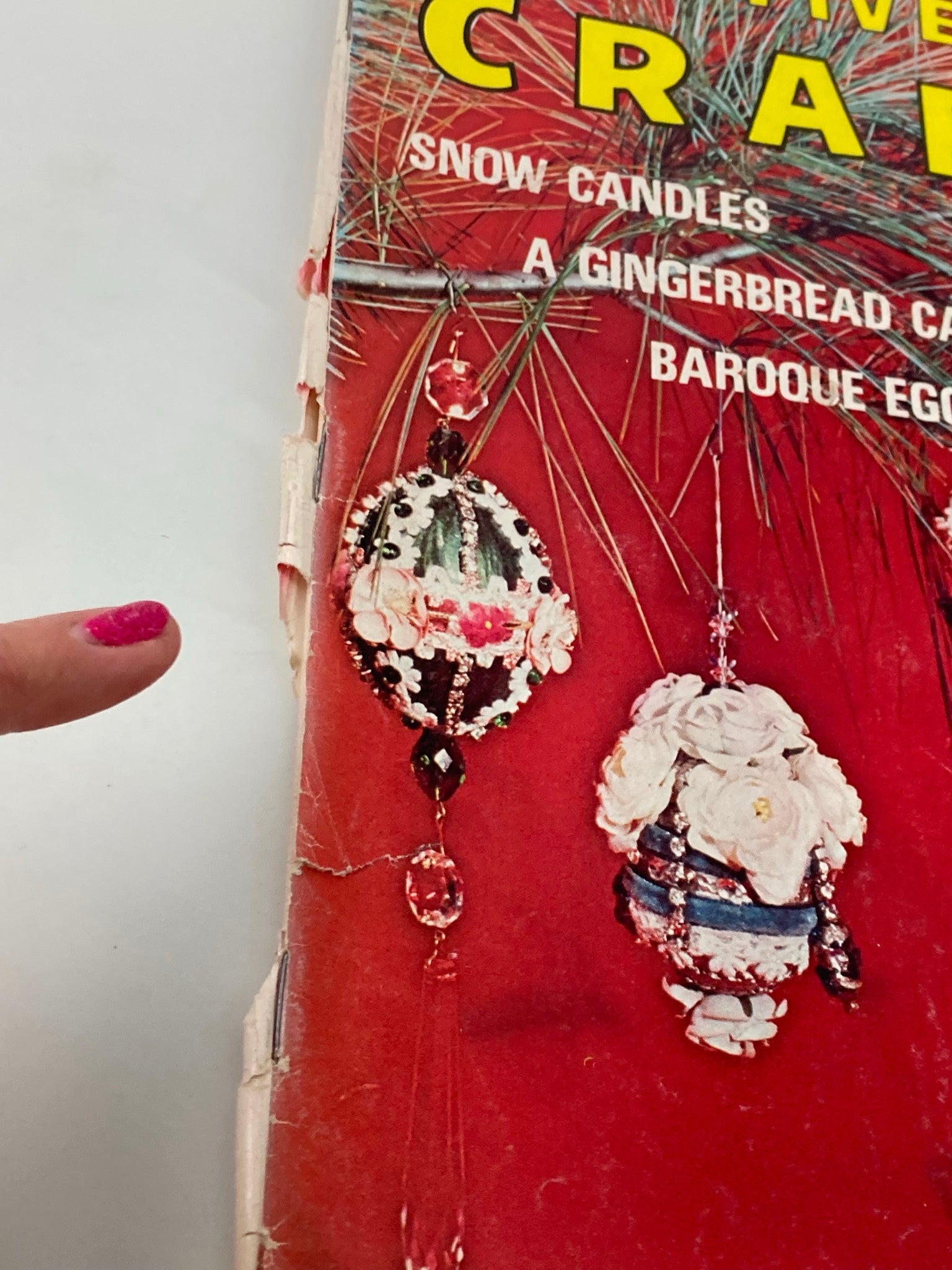 Close-up view of VTG Creative Crafts Magazine December 1974 cover highlighting decorative ceramic bells and floral designs alongside a person's finger pointing to the craft details.