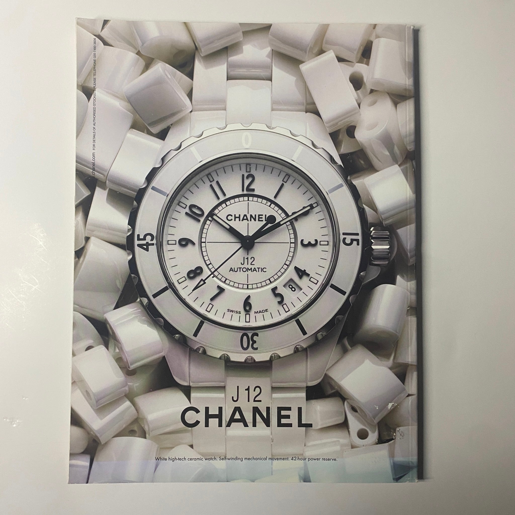 Chanel J12 Automatic watch featured in Harper's Bazaar Magazine June 2010. The watch is presented against a backdrop of white accessories, showcasing its elegant design.