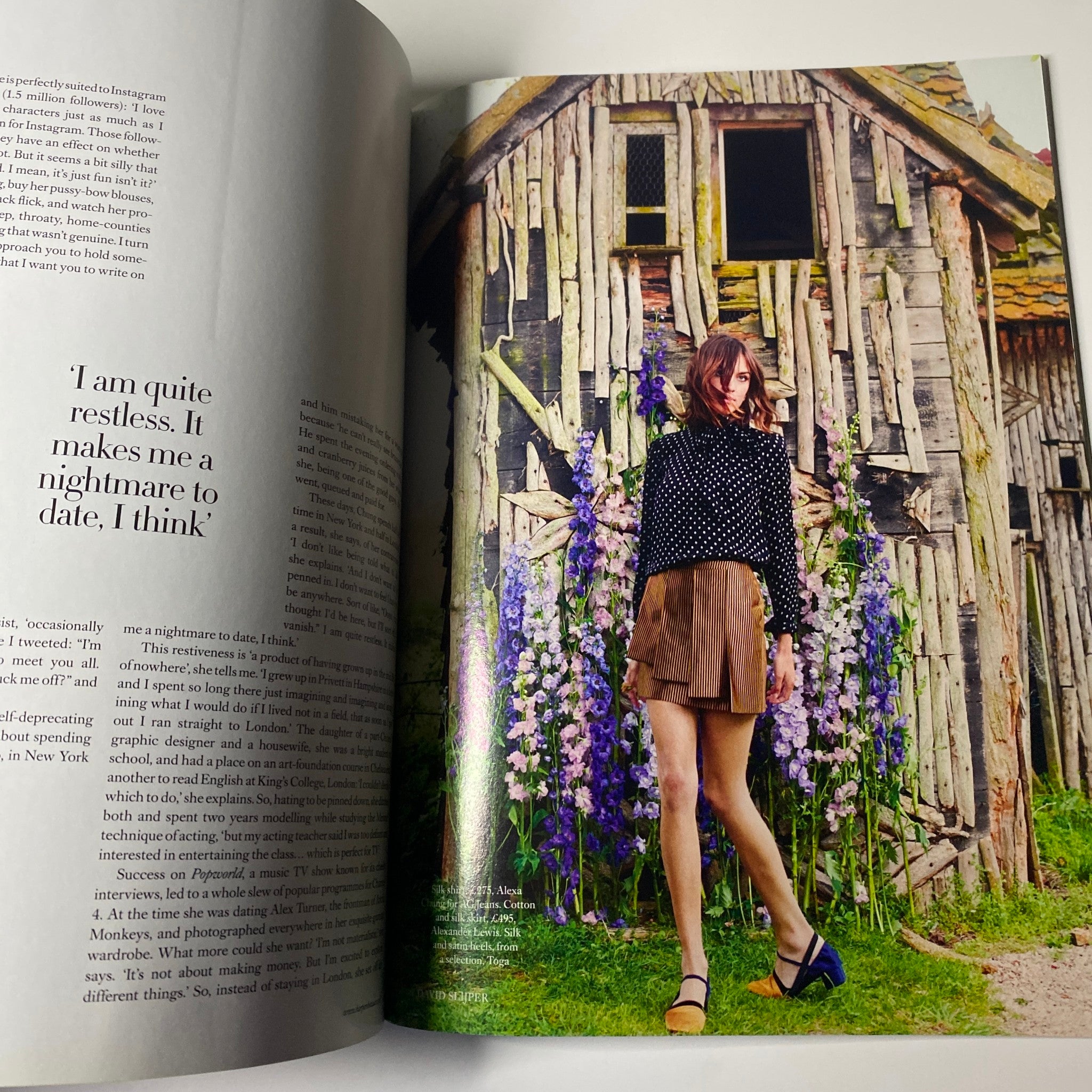 Fashion editorial image of a model wearing a polka dot top and skirt standing in front of a rustic building, featured in Harper's Bazaar UK Magazine July 2015 Alexa Chung Cover No Label VG.