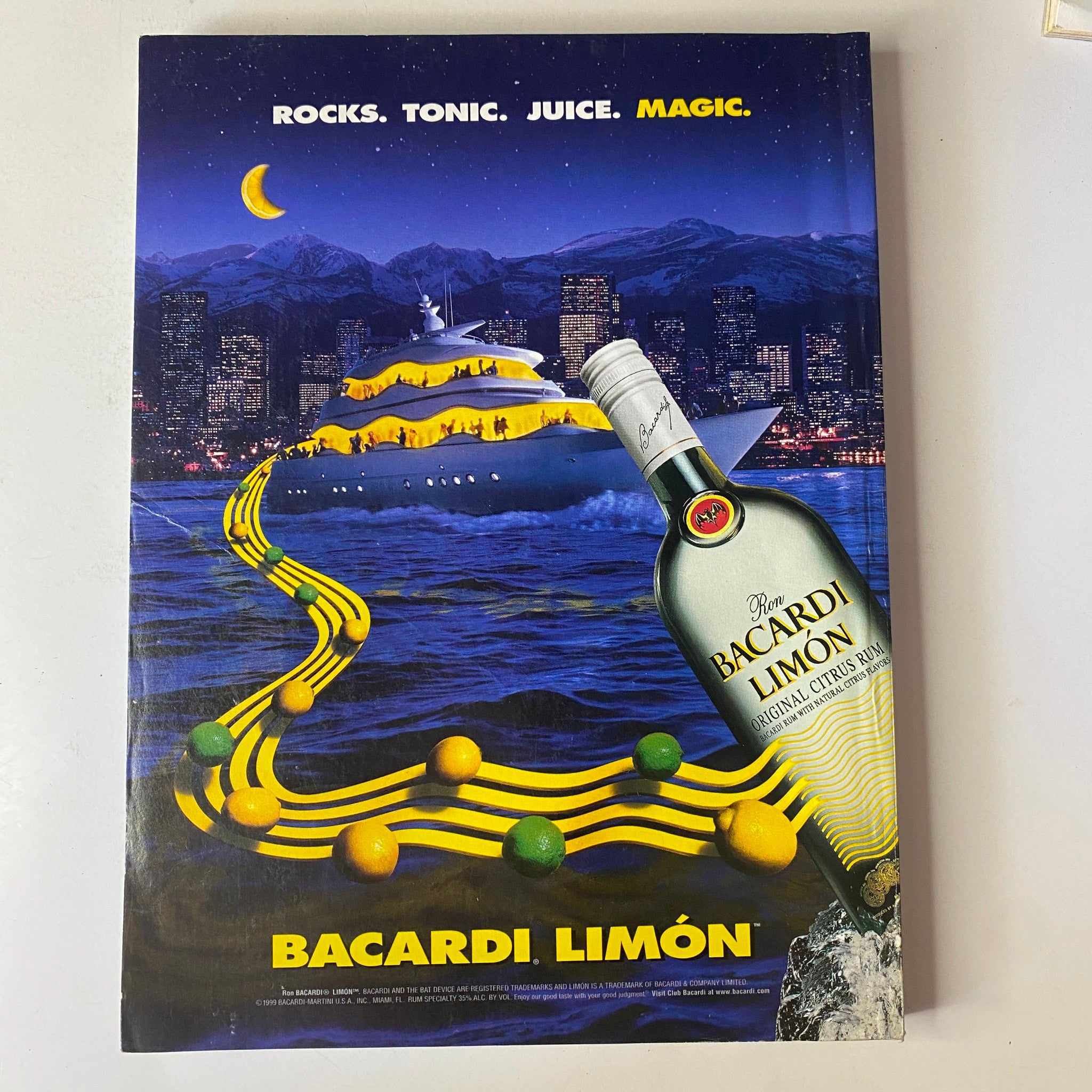 Bacardi Limón advertisement featuring a vibrant illustration of a yacht on the water, surrounded by urban scenery, along with the phrase 'Rocks. Tonic. Juice. Magic.' The ad promotes Bacardi Limón, highlighting its refreshing lemon-flavored rum.