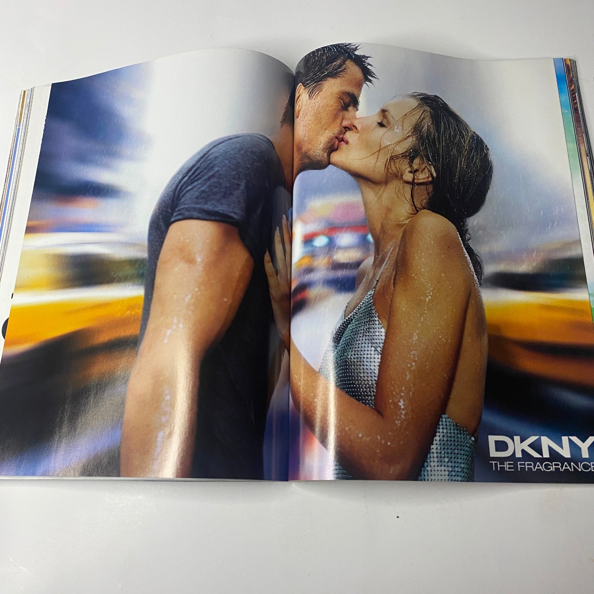 Advertisement spread from Vogue Magazine April 2000 featuring a romantic DKNY fragrance campaign, showcasing a couple in a passionate kiss amidst a dynamic urban backdrop.