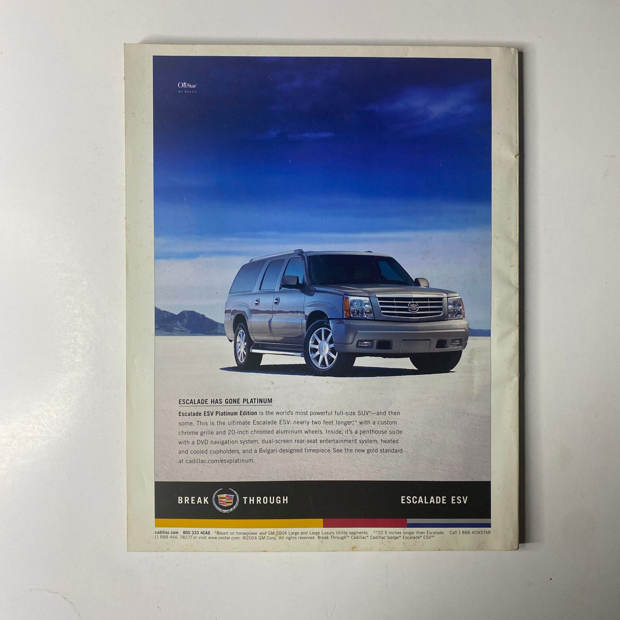 Advertisement for the Cadillac Escalade ESV, featuring a sleek silver SUV against a scenic blue sky backdrop, showcasing its luxury and power. This image corresponds with the title 'Ebony Magazine August 2004 Halle Berry Cover'.