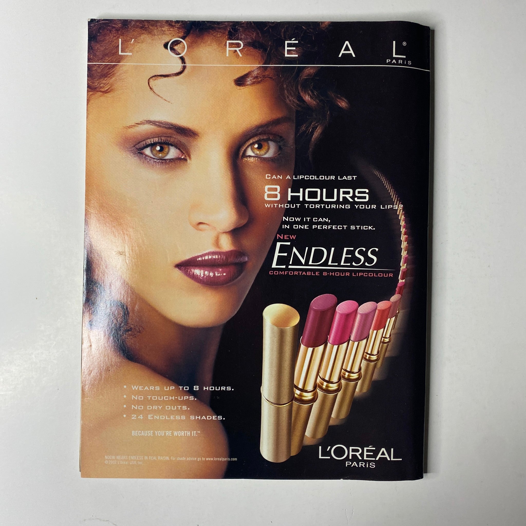 L'Oreal Paris advertisement showcasing a model with curly hair and a selection of lipsticks, featured in Ebony Magazine August 2002 Vol. LVII, No. 10.