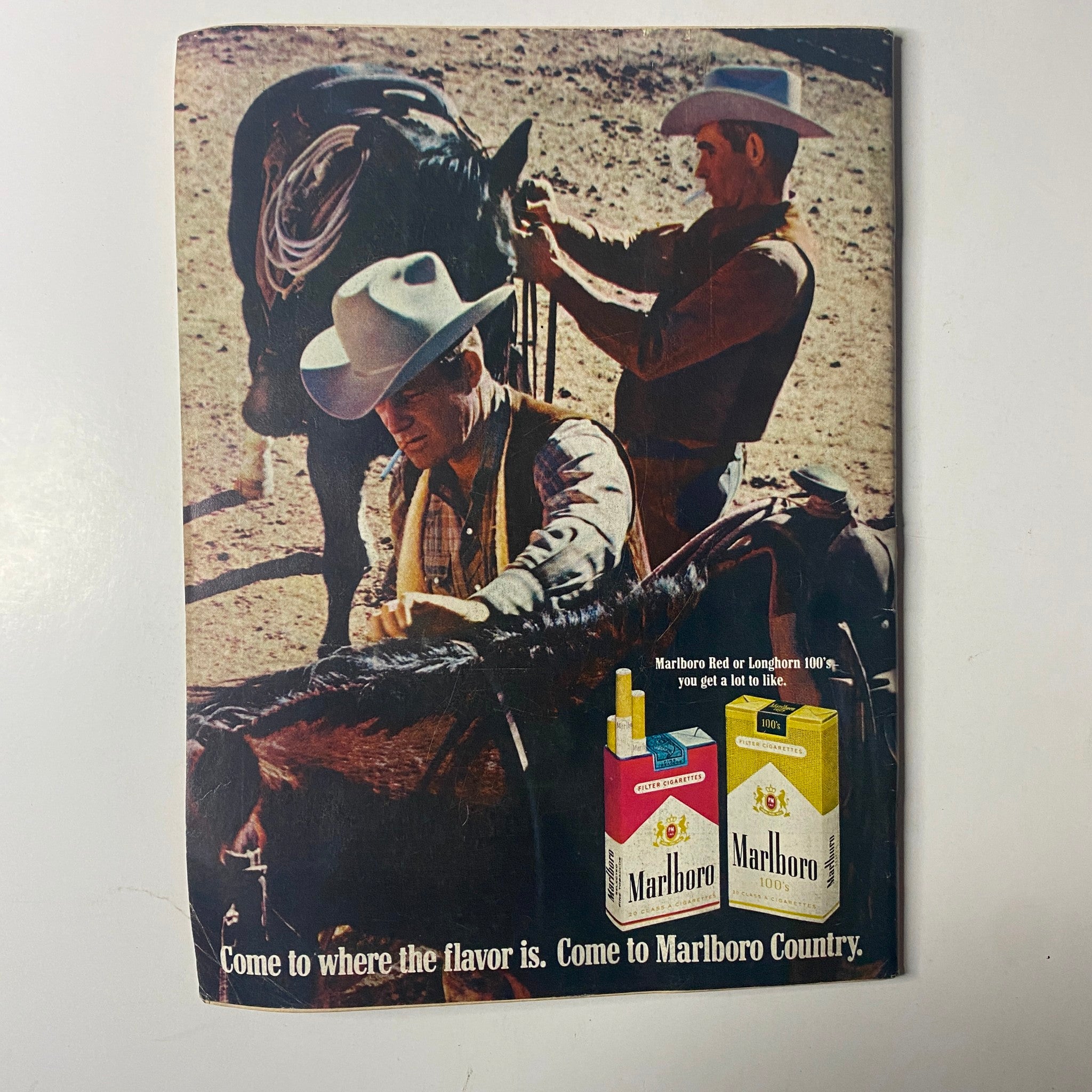 Vintage advertisement for Marlboro featuring two cowboys with a horse, promoting Marlboro cigarettes, capturing the essence of cowboy culture.