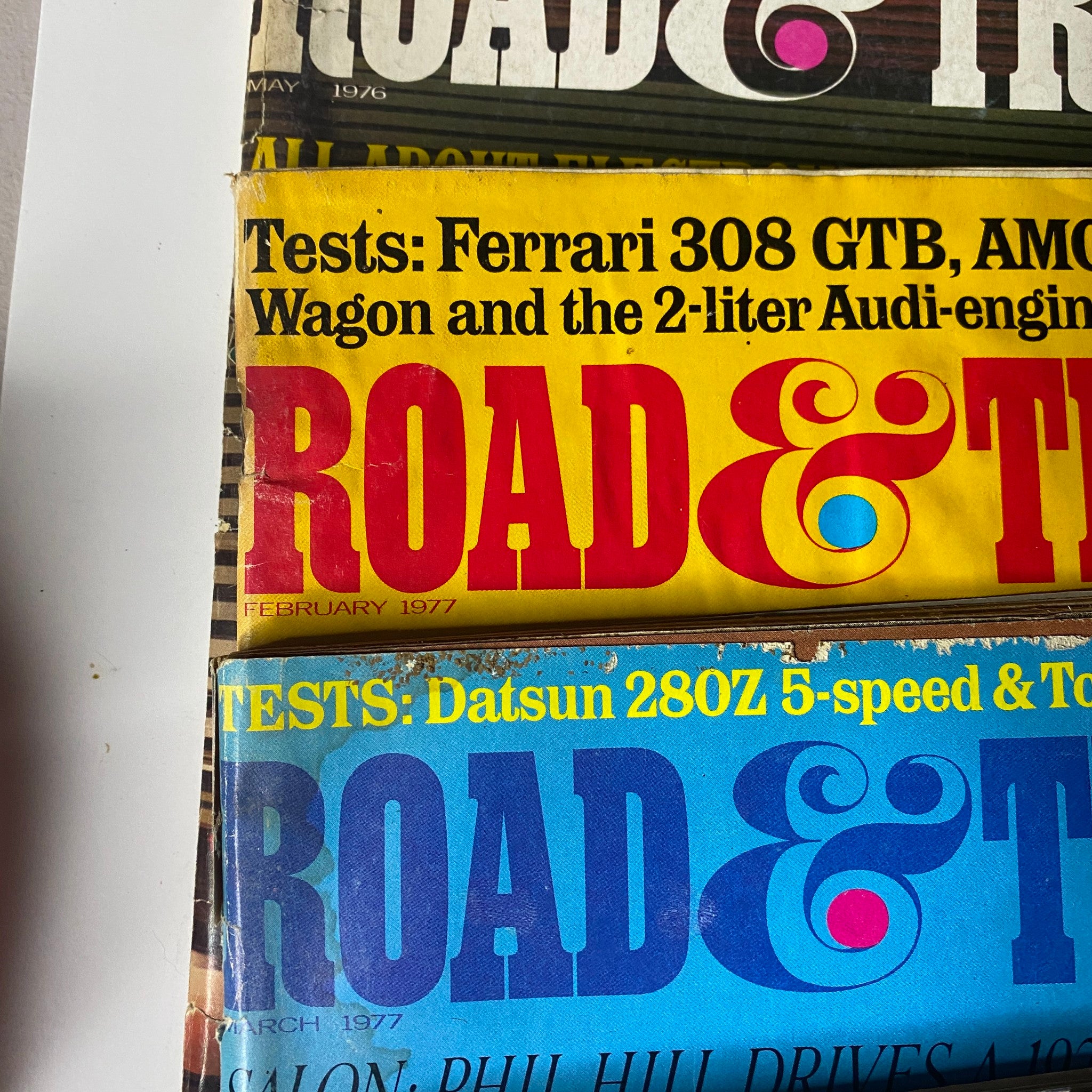 Close-up view of Road & Track Magazine covers from February 1977 and March 1977, including tests on Ferrari 308 GTB and Datsun 280Z models.
