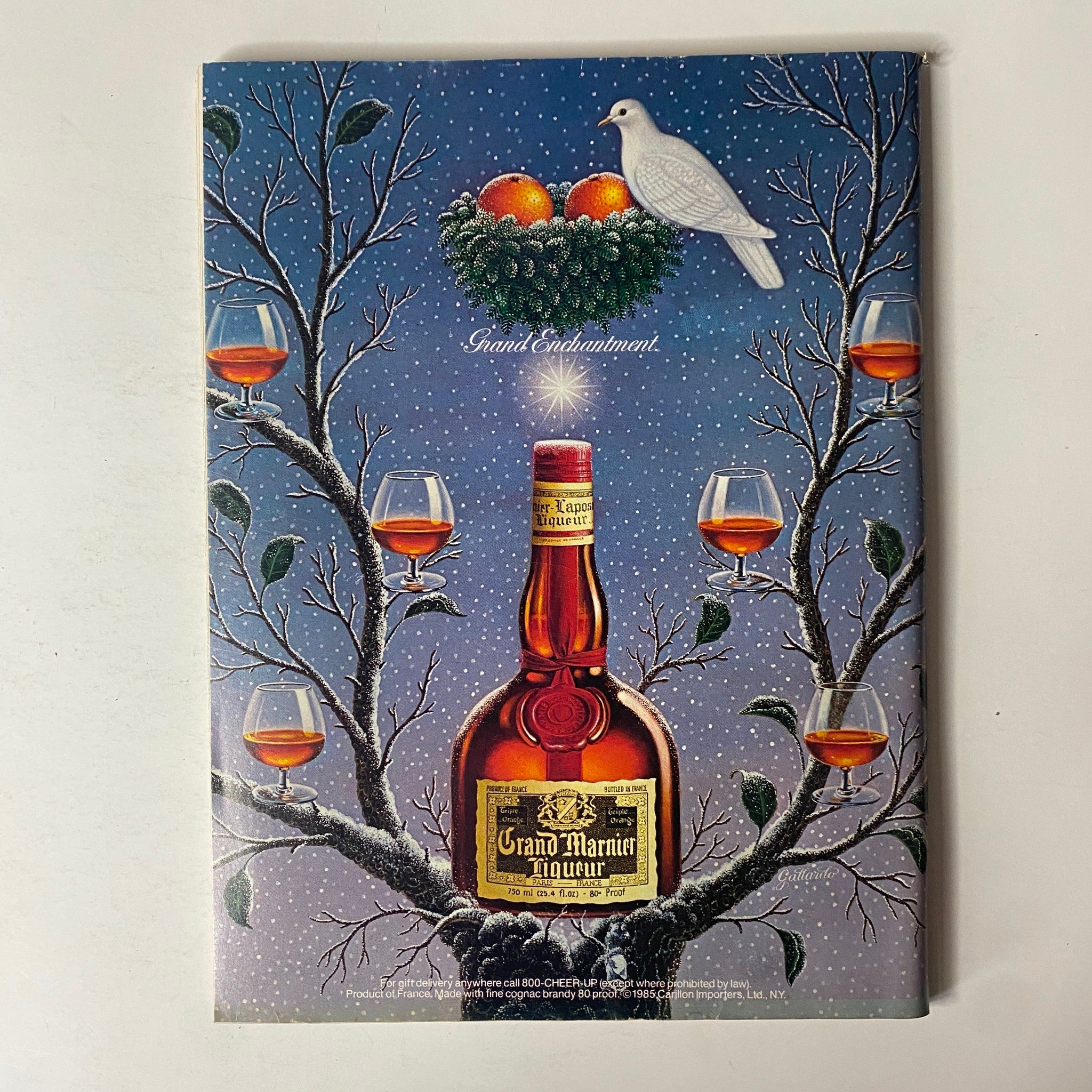 Artistic advertisement for Grand Marnier liqueur featuring a bottle amidst winter scenery with glasses of liqueur on branches, titled 'Forbes Magazine December 16, 1985 Spendthrift America? The Myth Exposed'.