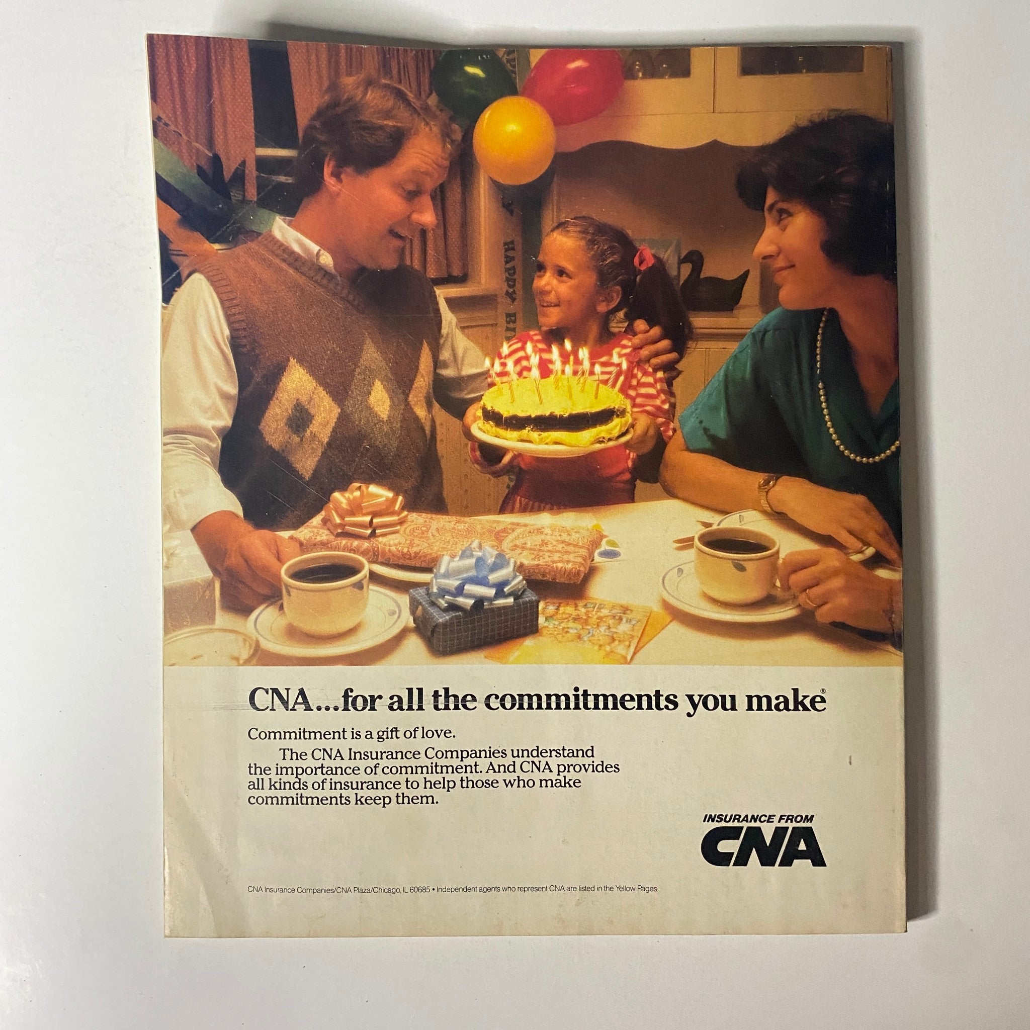 CNA advertisement featuring a family celebrating a birthday with cake and gifts. The image includes a man and a woman enjoying the occasion with a young girl holding a cake, reflecting the theme 'CNA...for all the commitments you make'. This vintage advertisement highlights commitment as a gift of love, relevant to the context of insurance.