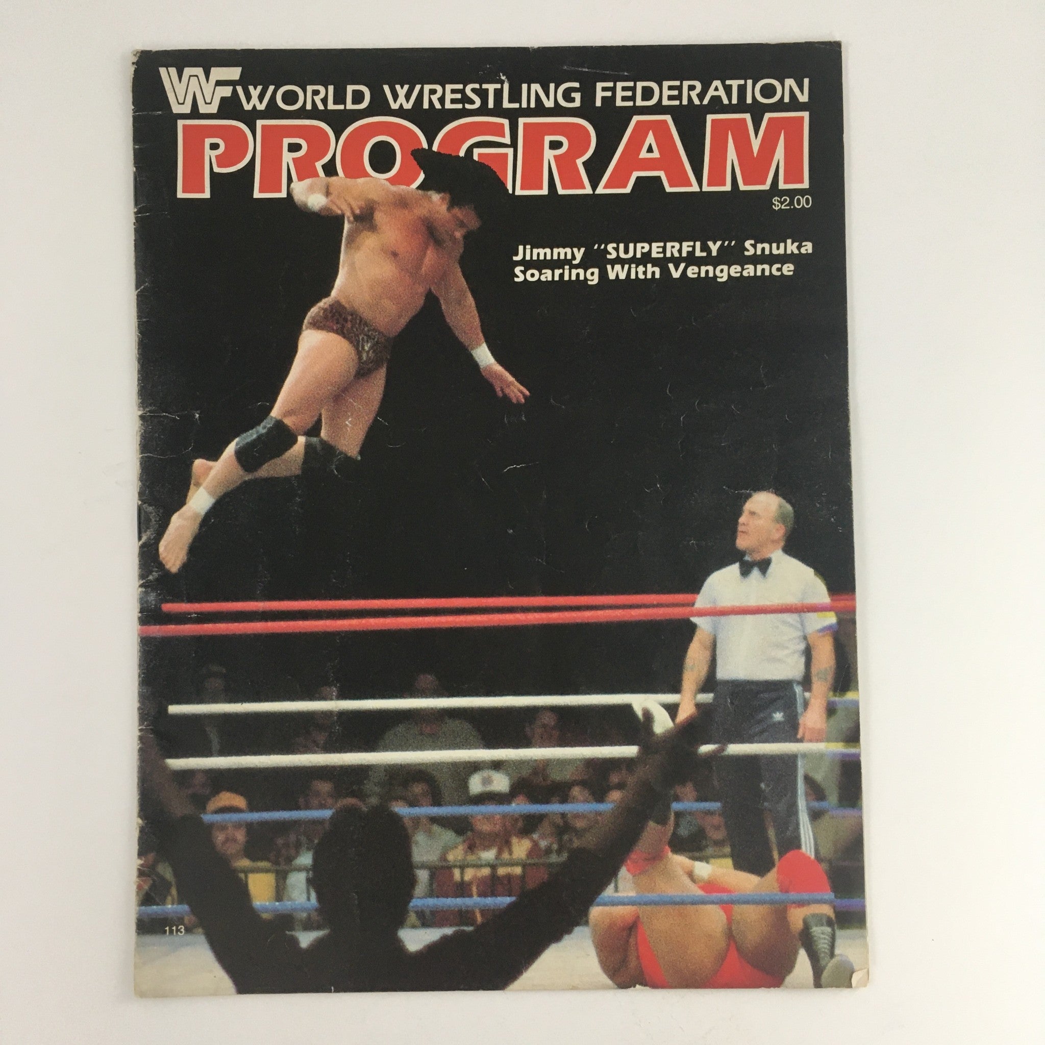 WWF Program #113 June 23 1984 with featured wrestling action of Jimmy 'SUPERFLY' Snuka soaring in the air during a match against Mr. Wonderful and referee in the ring.