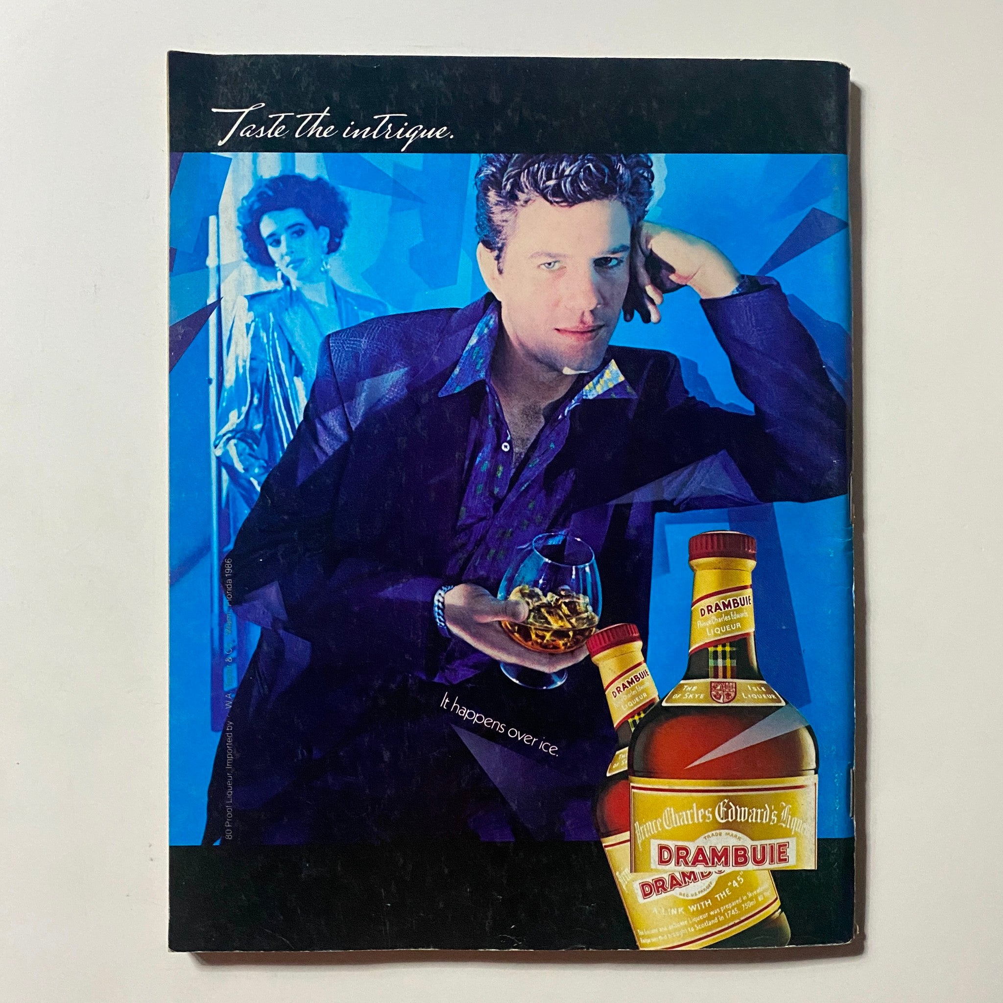 Cover page of a vintage advertisement featuring Drambuie liqueur, showcasing a stylish man and a woman with a tagline 'It happens over ice'.