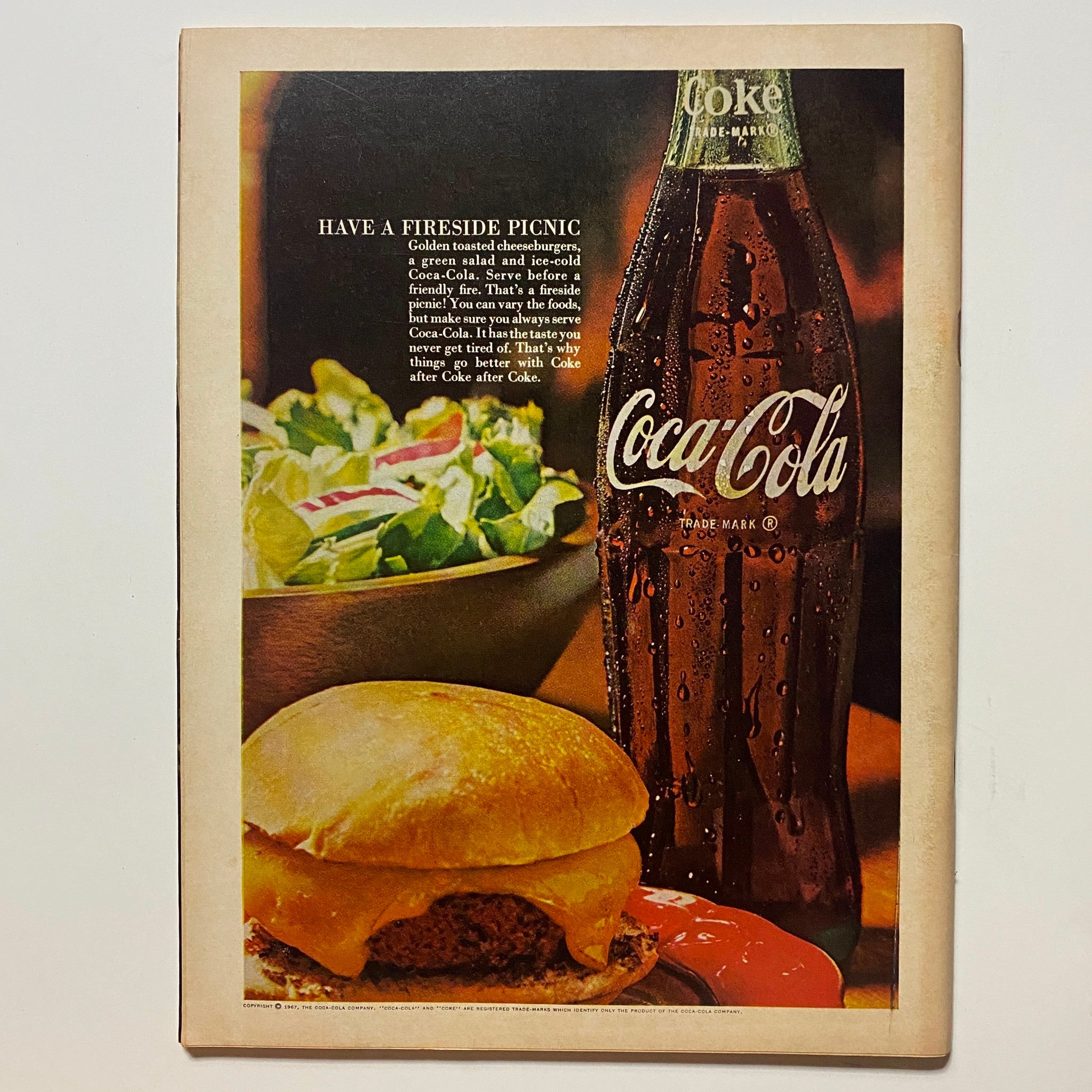 Vintage advertisement featuring a Coca-Cola bottle next to a cheeseburger and salad with the caption 'Have a Fireside Picnic'. This image complements the VTG Hot Rod Magazine January 1967 Bolt-On Gurney Weslake Heads No Label, emphasizing classic American dining culture.