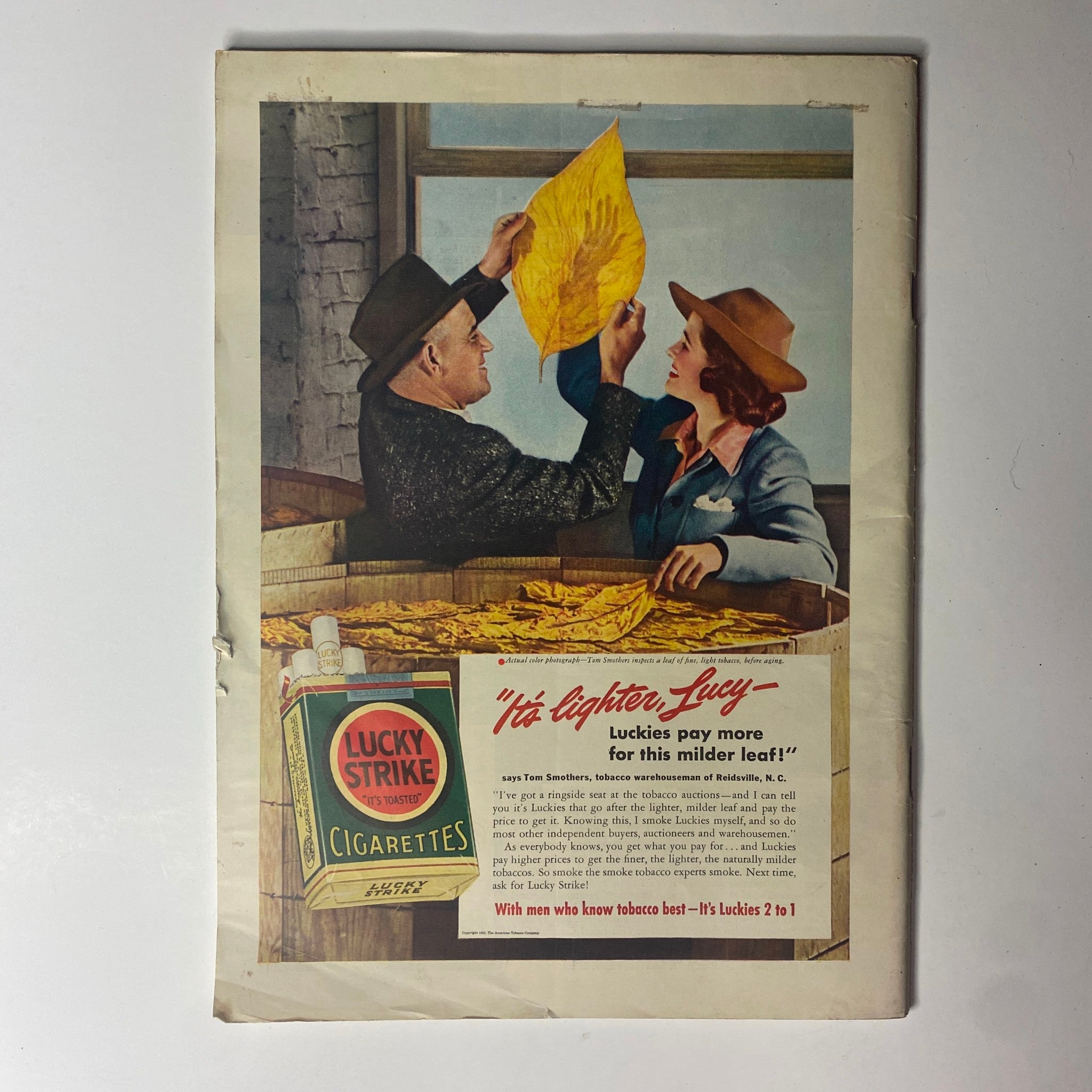 Vintage advertisement for Lucky Strike cigarettes from a historical magazine, featuring characters discussing tobacco quality. The ad emphasizes the lighter nature of Lucky Strikes, complementing the theme of pricing and economy related to the magazine issue.