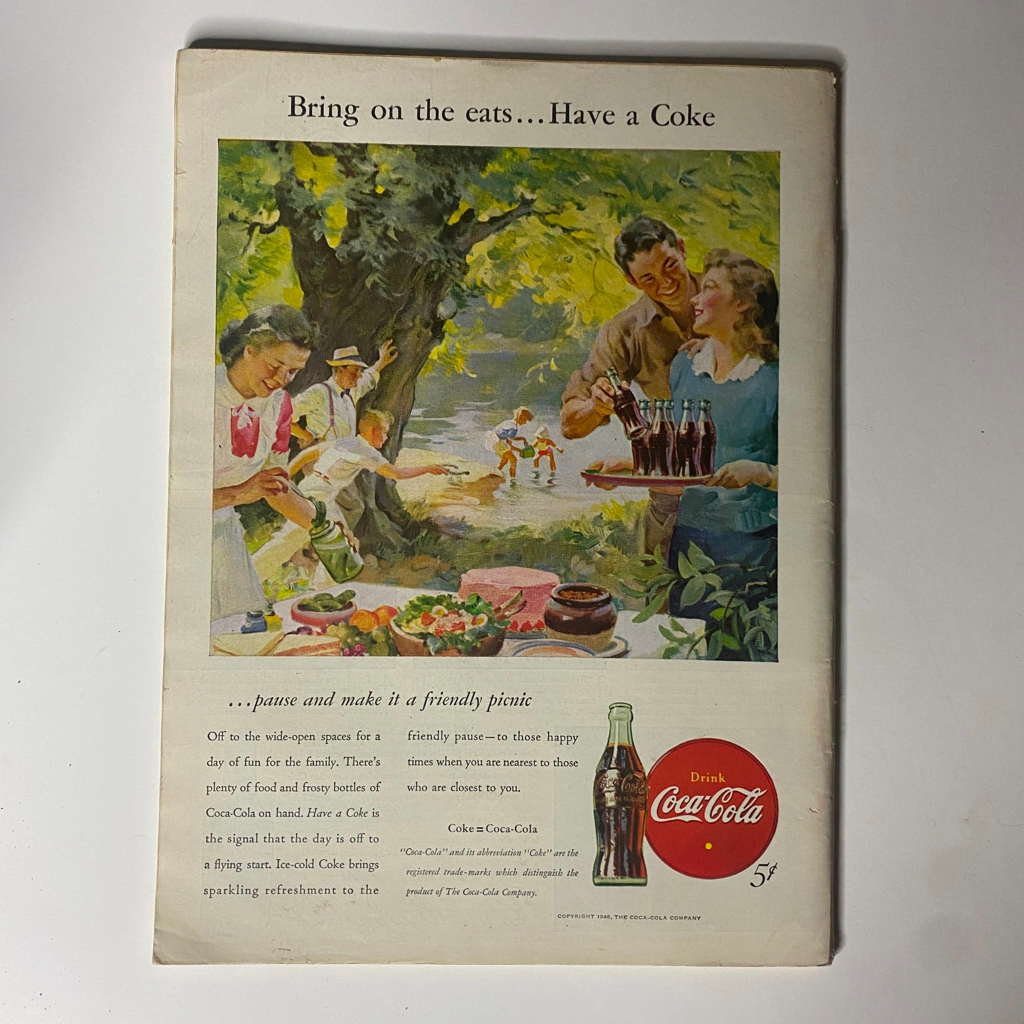 Vintage advertisement for Coca-Cola promoting friendly picnic gatherings. The image depicts people enjoying a picnic in nature, serving food and drinks.