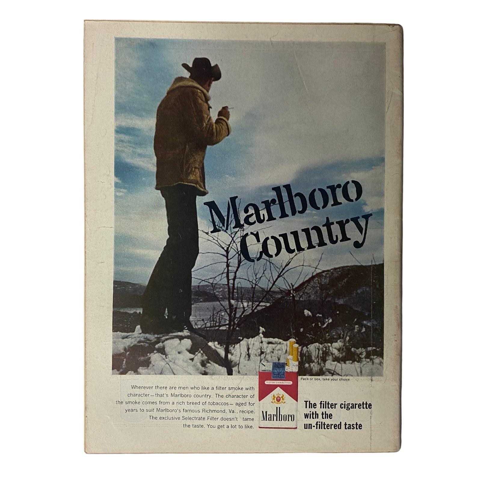 Vintage Marlboro advertisement showcasing a lone cowboy in a winter landscape, promoting Marlboro Country cigarettes, illustrating a rugged outdoor lifestyle.