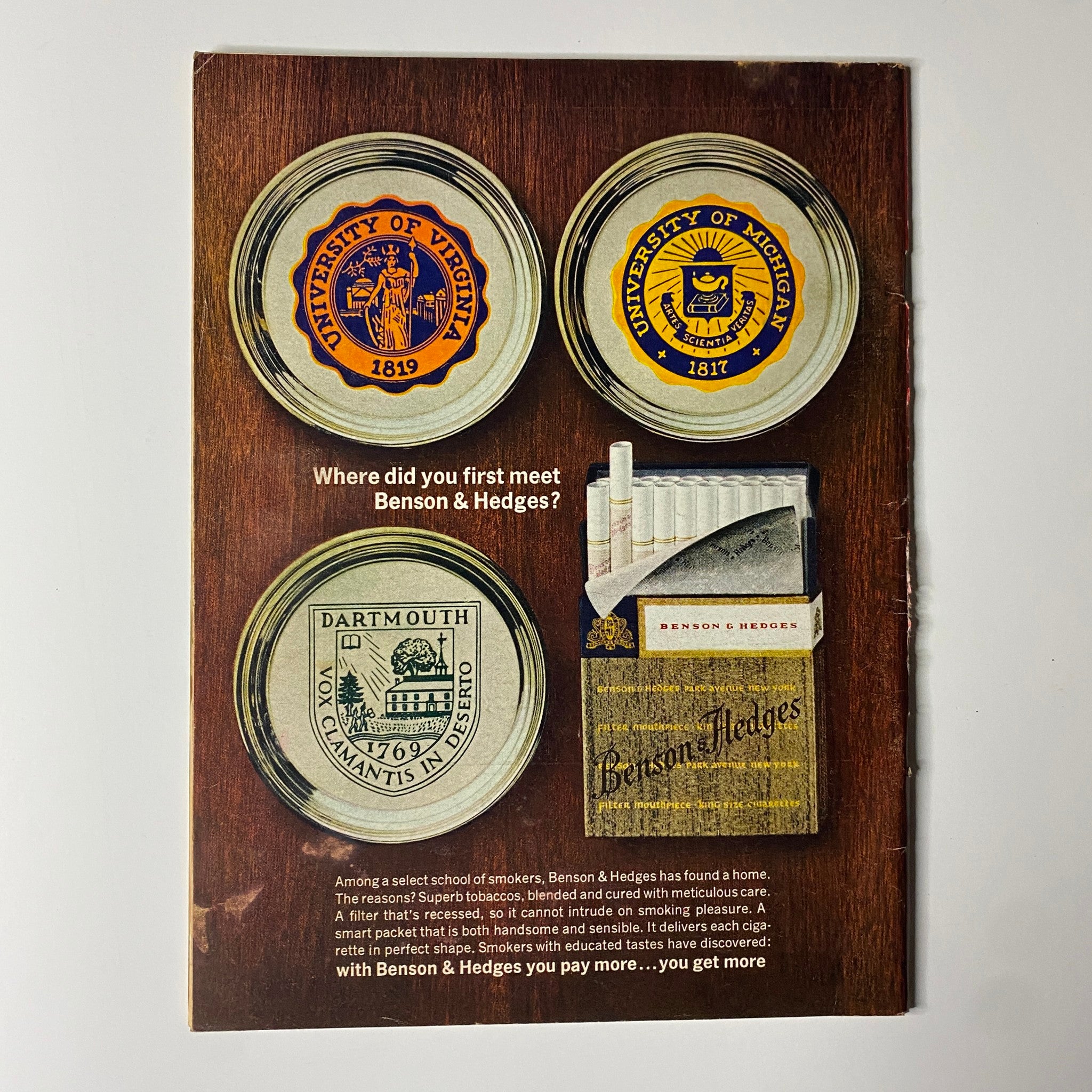 Retro advertisement for Benson & Hedges featuring a collection of academic seals from universities including the University of Virginia, University of Michigan, and Dartmouth, with the tagline 'Where did you first meet Benson & Hedges?'. This vintage design illustrates brand heritage and the appeal to educated smokers.