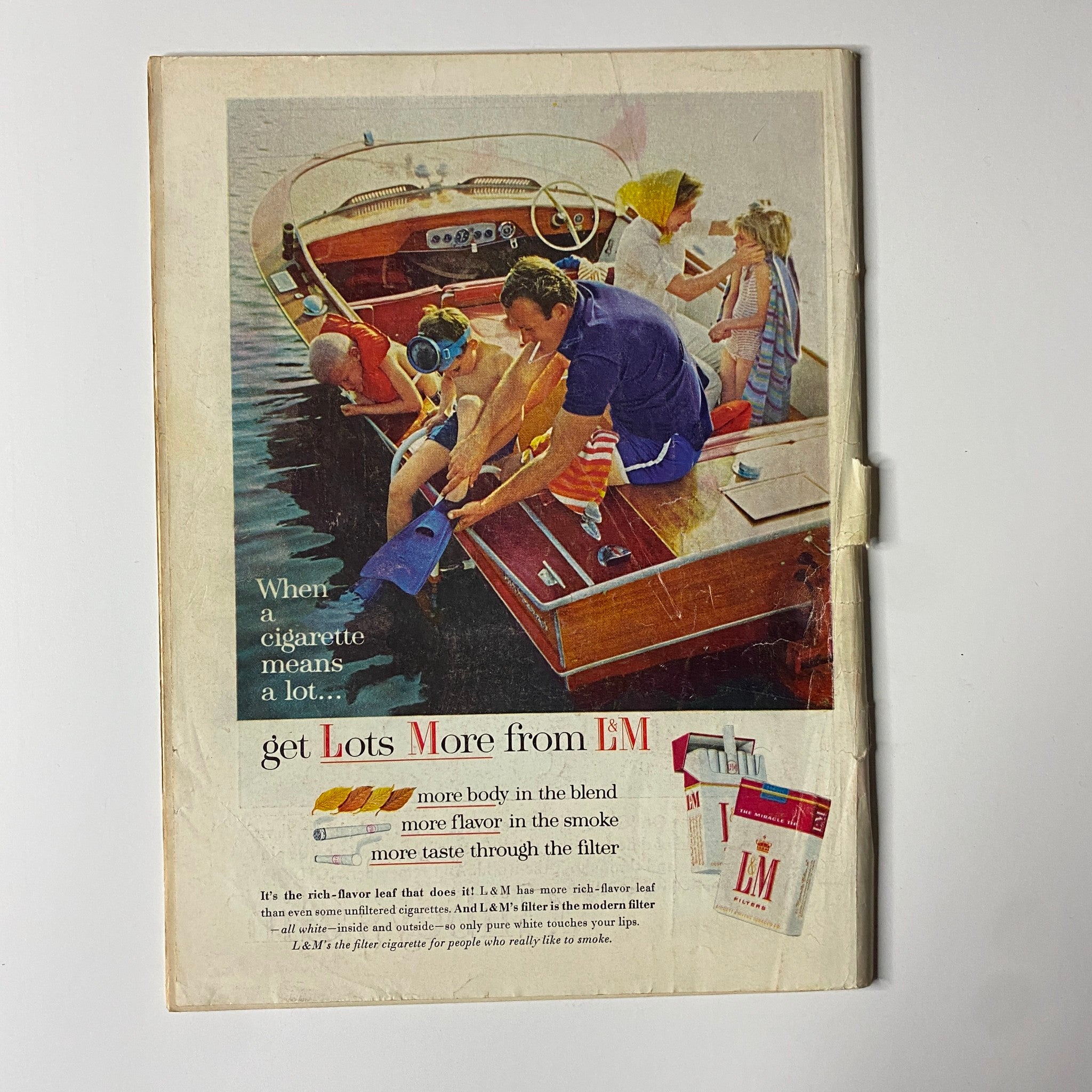 Back cover of a vintage magazine advertisement for L&M cigarettes, depicting a family enjoying a day on the water, promoting the cigarette brand's features.