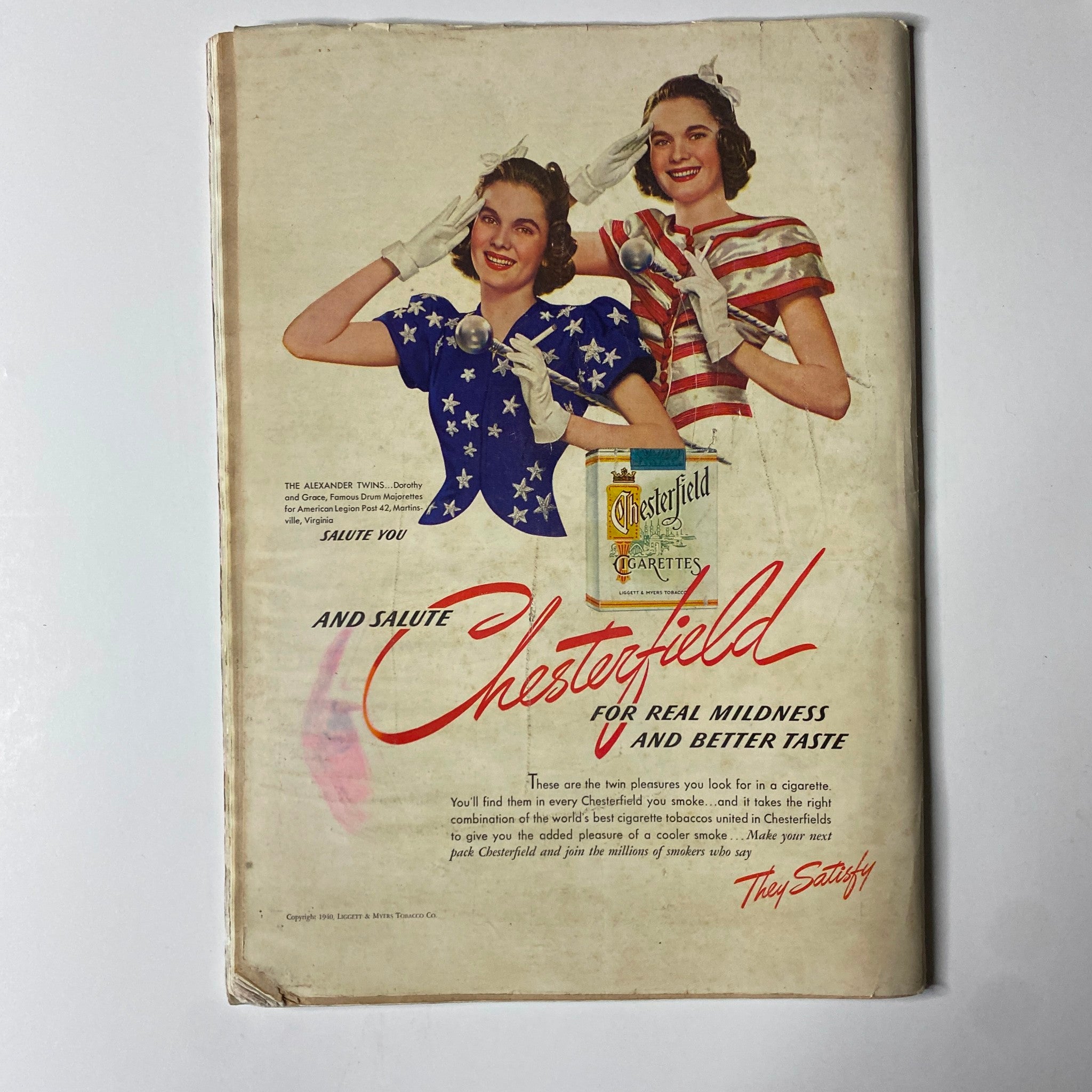Vintage advertisement for Chesterfield cigarettes featuring two women in patriotic outfits, saluting and promoting the brand from a nostalgic magazine.