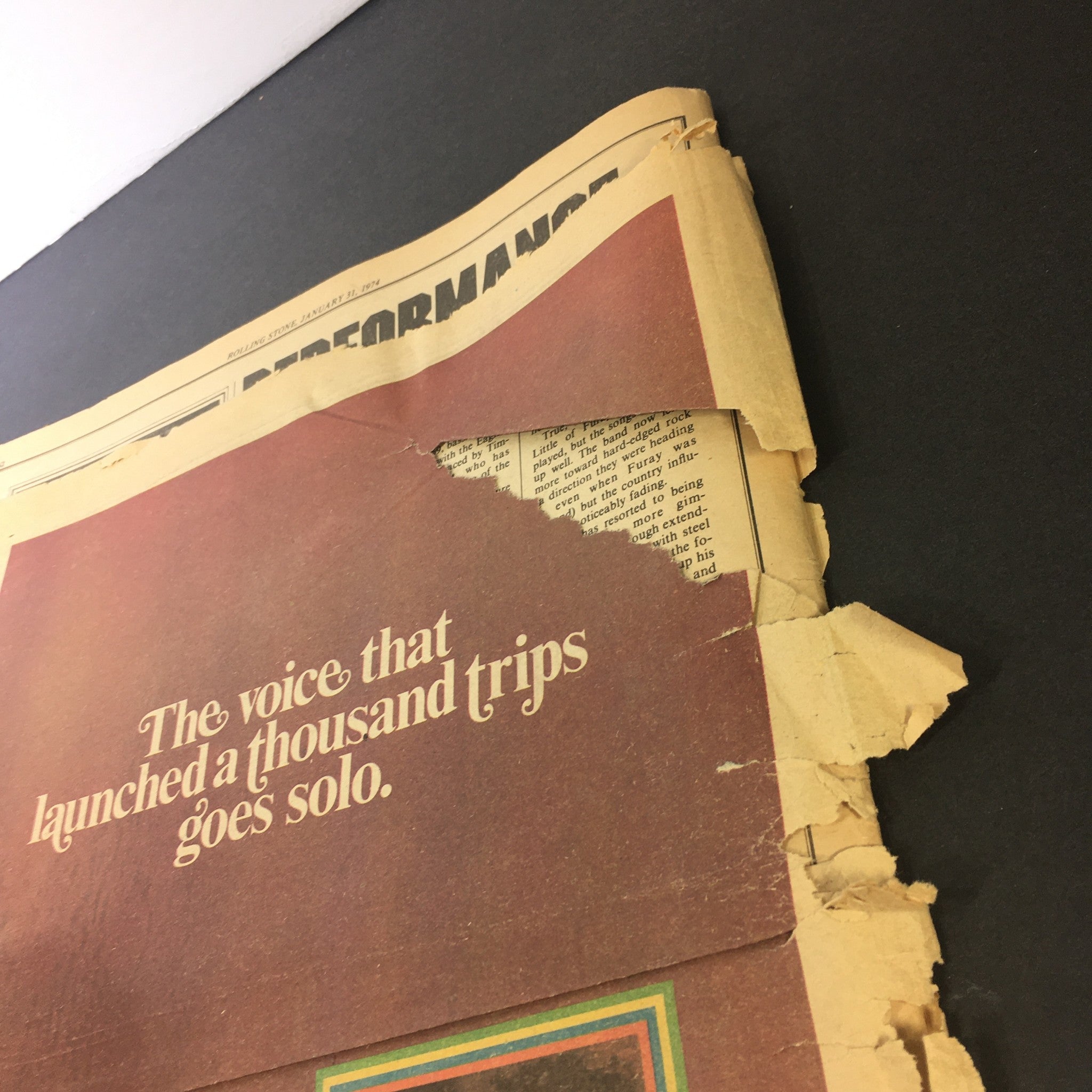 Image of the back cover of the vintage Rolling Stone magazine from January 31, 1974, displaying a partially torn page with text that reads, 'The voice that launched a thousand trips goes solo.' The condition indicates signs of age and use.