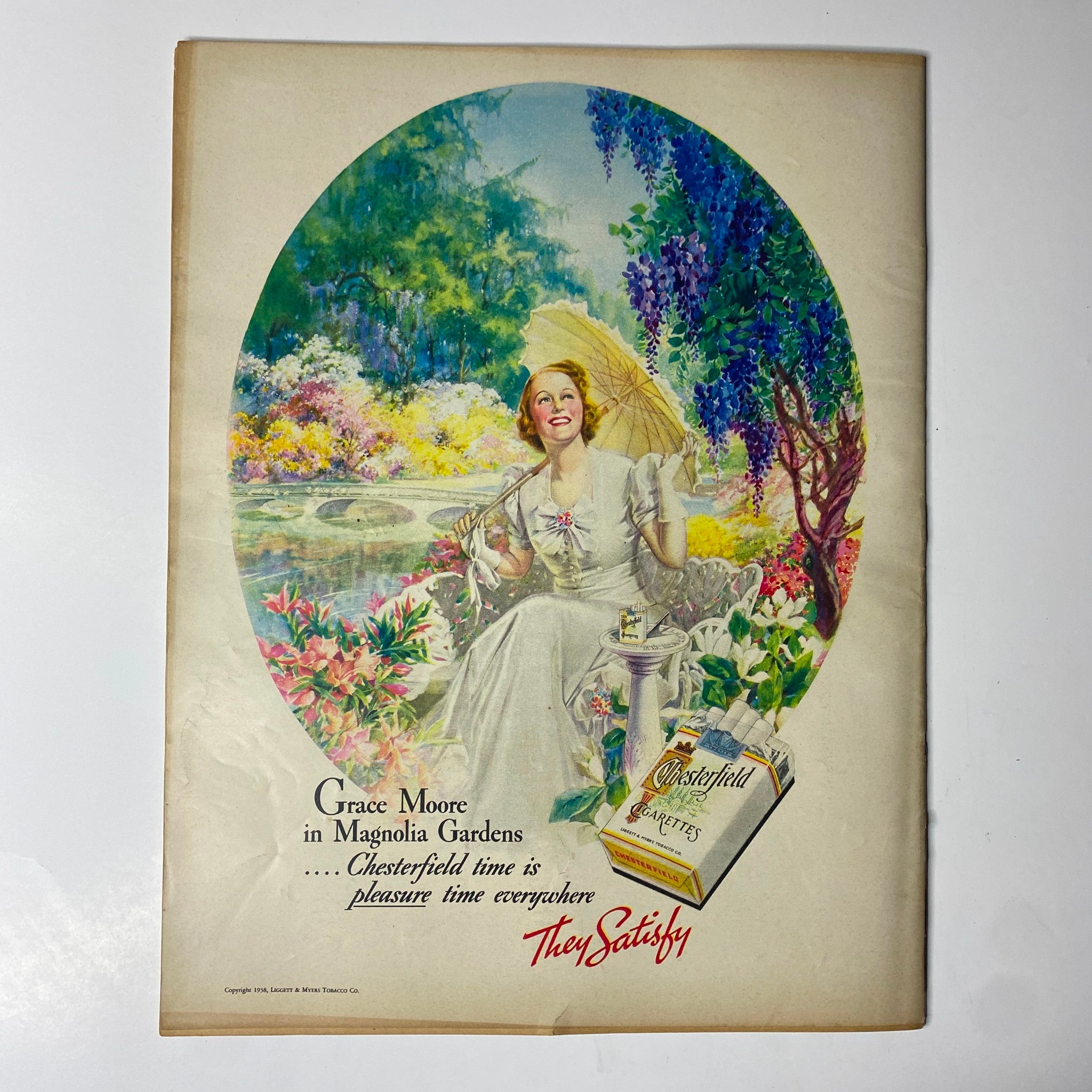 Advert featuring Grace Moore in Magnolia Gardens from Look Magazine, July 19, 1938. The colorful illustration depicts Moore joyfully holding an umbrella amidst a flourishing garden, promoting Chesterfield cigarettes with the slogan 'They Satisfy.'