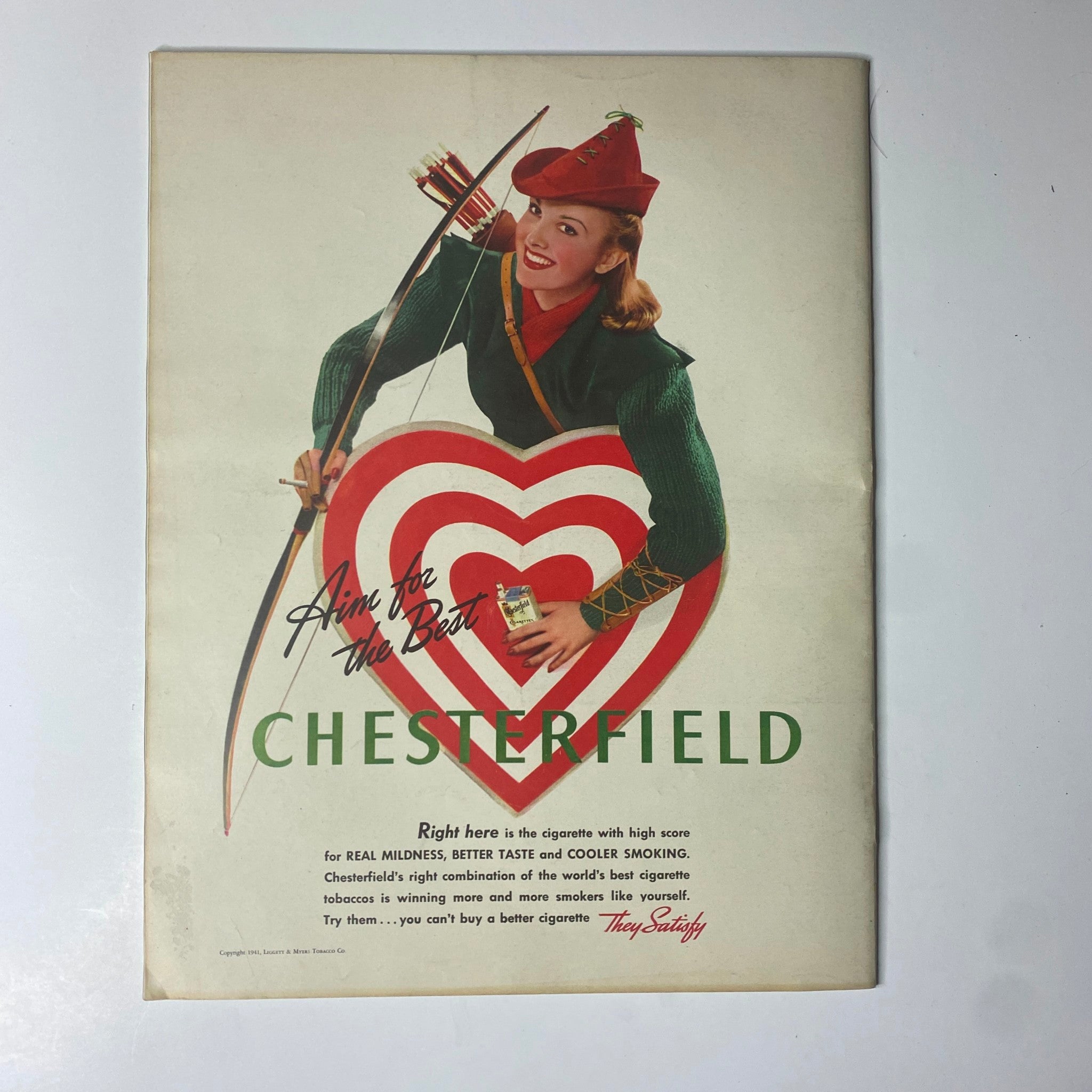 Vintage Chesterfield advertisement from Look Magazine February 25, 1941 featuring a model in a festive outfit holding a large heart-shaped illustration with a bow and arrow, promoting the brand.