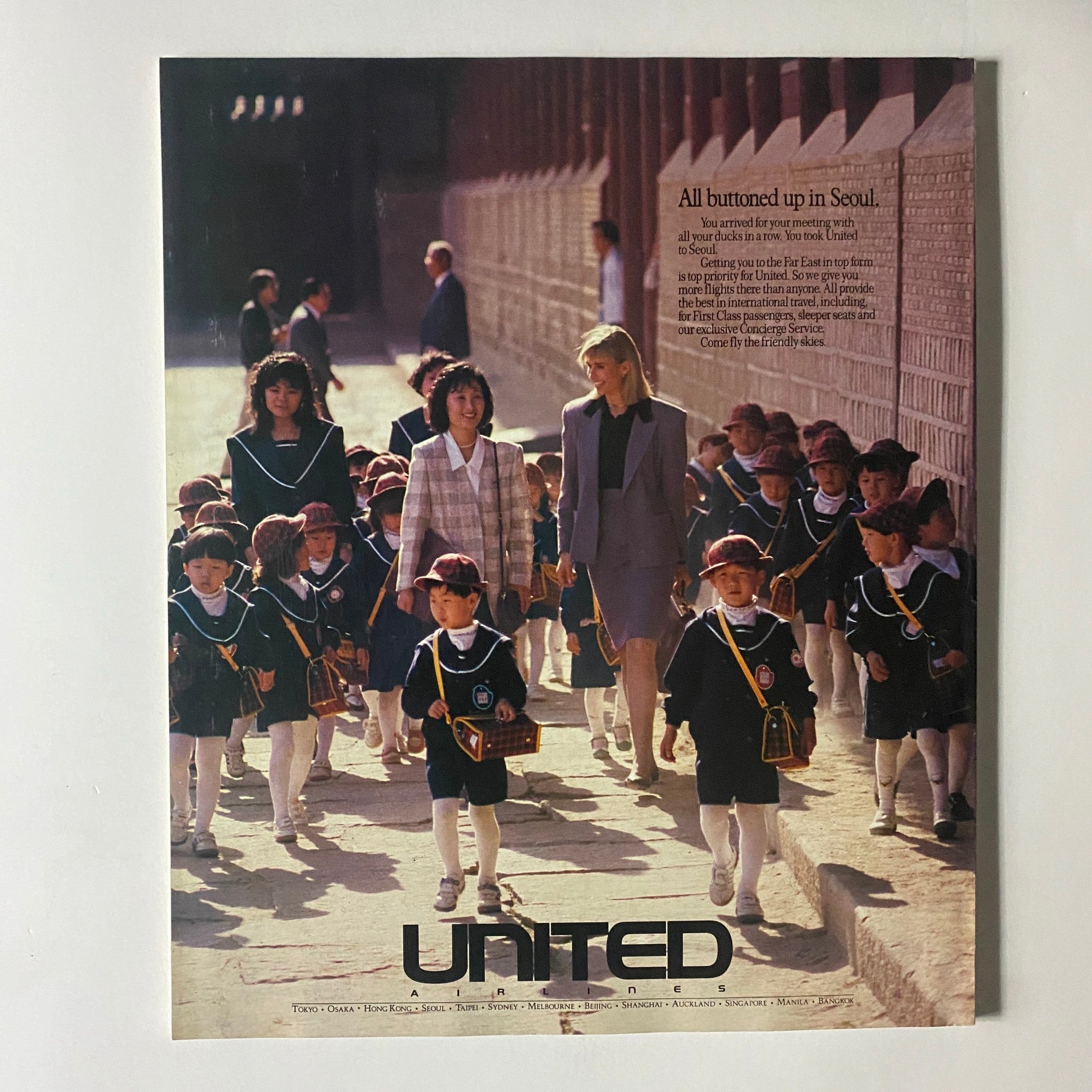 Vintage advertisement featuring United Airlines, showcasing a sophisticated scene in Seoul with children in school uniforms and women in professional attire.