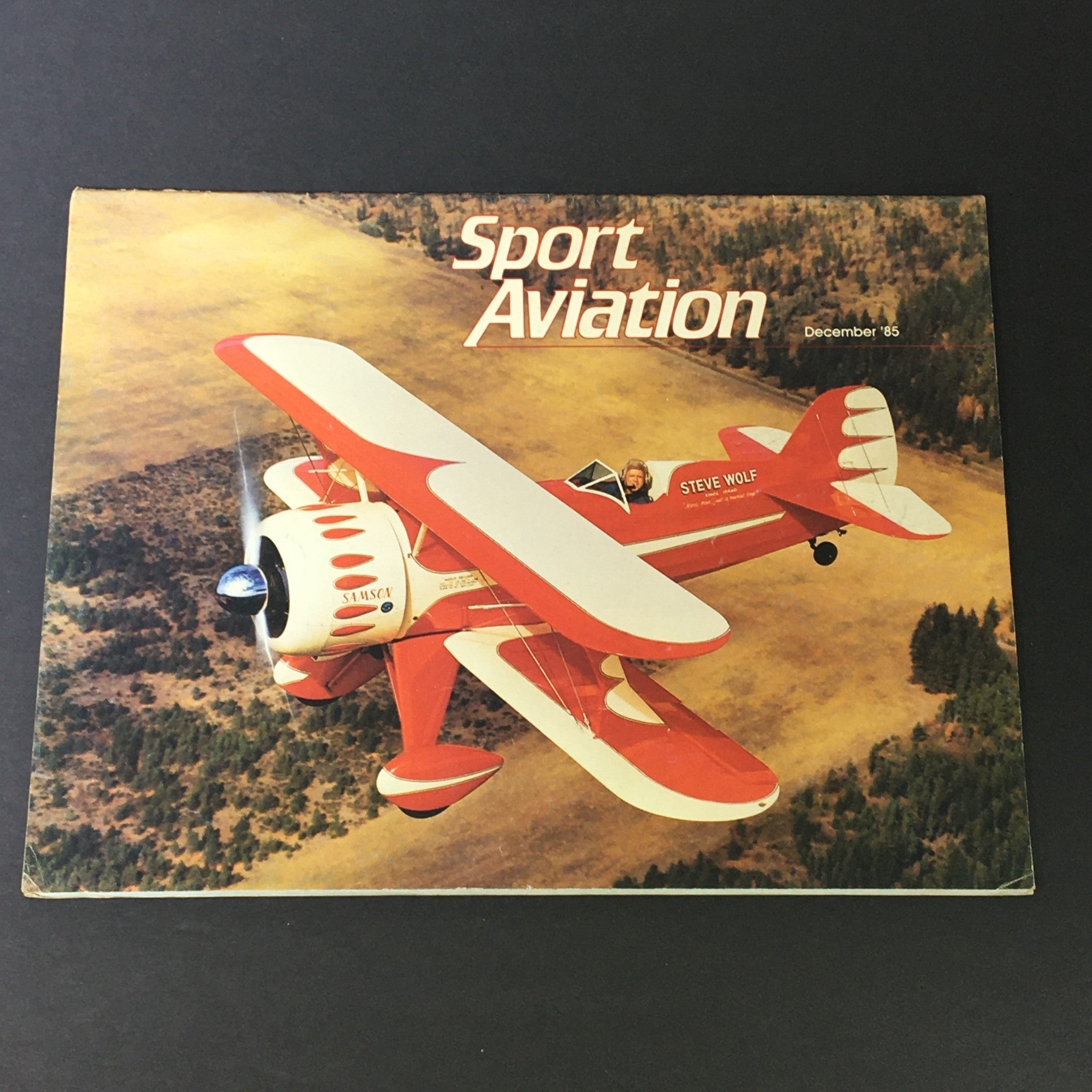 Vintage Sport Aviation Magazine December 1985 cover featuring a red biplane in flight over a scenic landscape, showcasing the vibrant world of sport aviation.