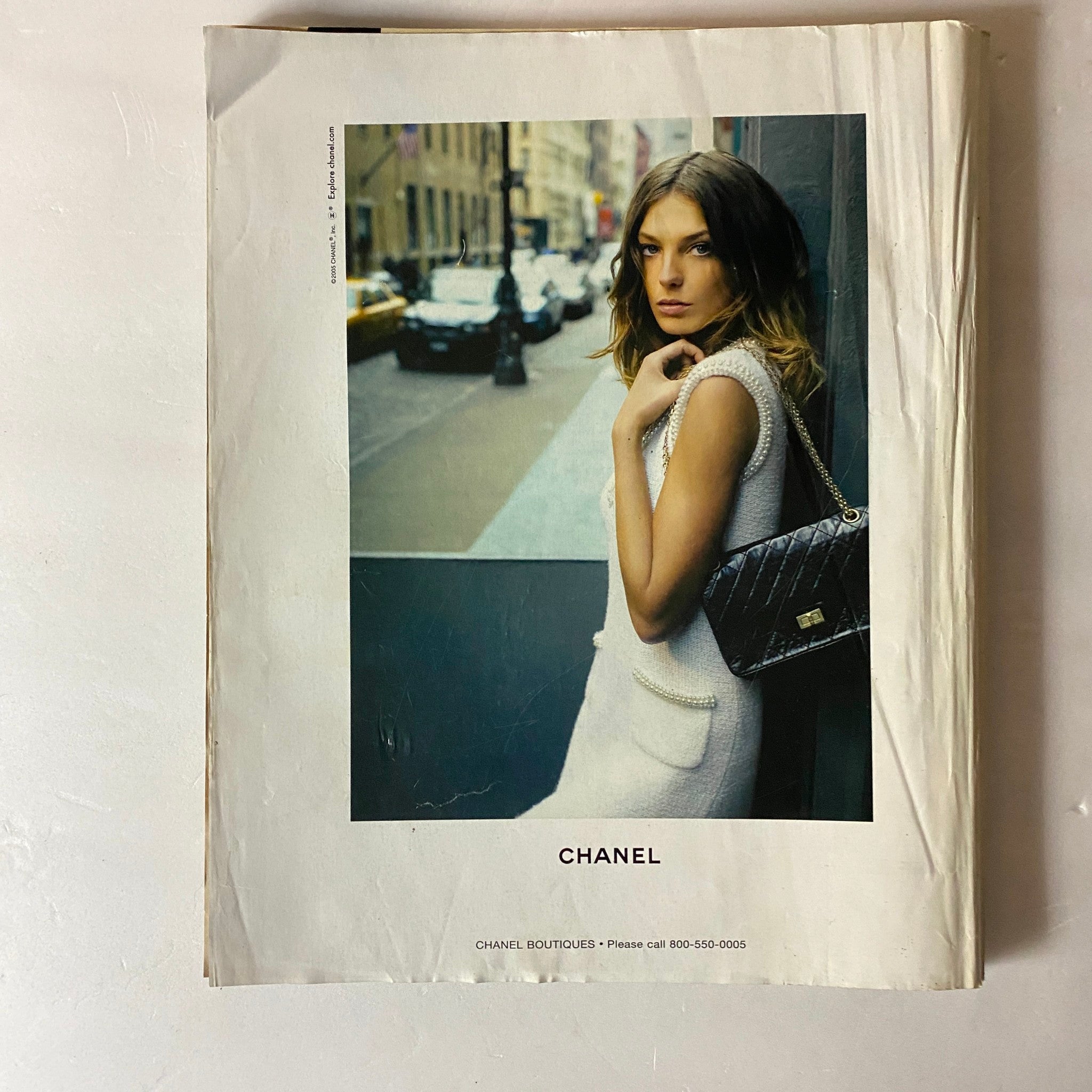 An advertisement from The New York Times Style Magazine 2005 featuring a model elegantly dressed in Chanel, standing against an urban backdrop, embodying the chic and sophisticated aesthetic of the magazine's Tilda Swinton cover.