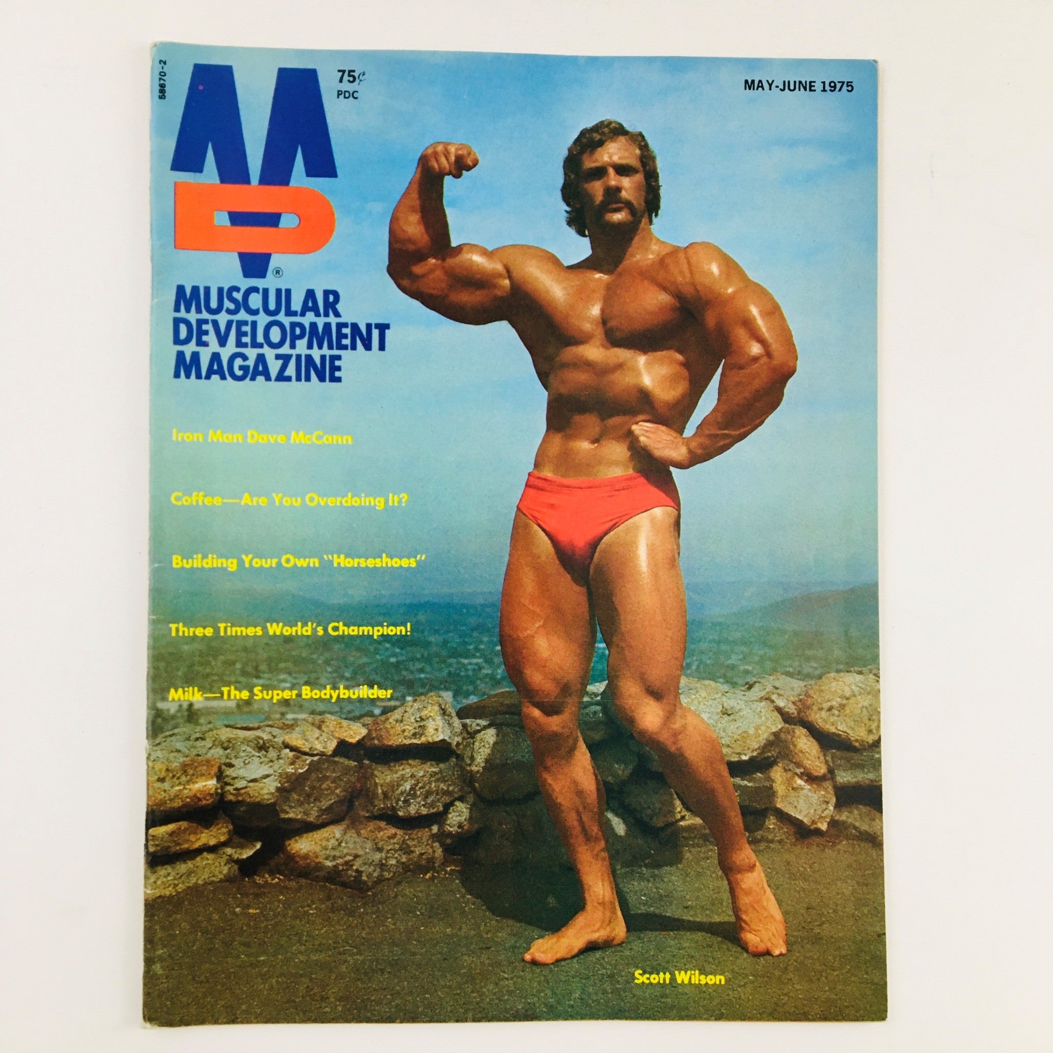 Cover of Muscular Development Magazine May 1975 featuring Scott Wilson in red swim trunks posing against a scenic background, showcasing the bodybuilding culture of the mid-1970s.