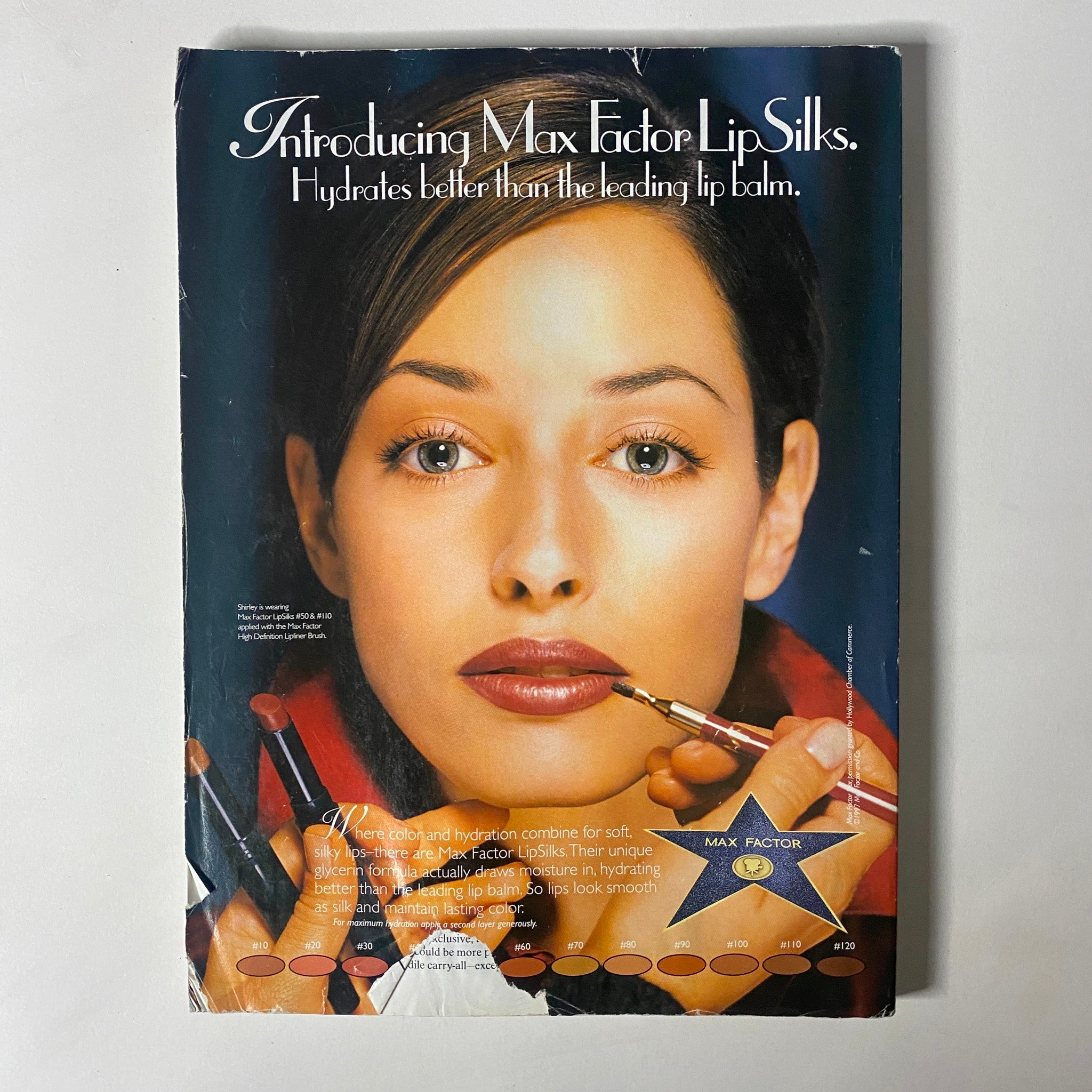 Advertisement from Vogue Magazine August 1997 introducing Max Factor LipSliks with a beauty model demonstrating makeup application.