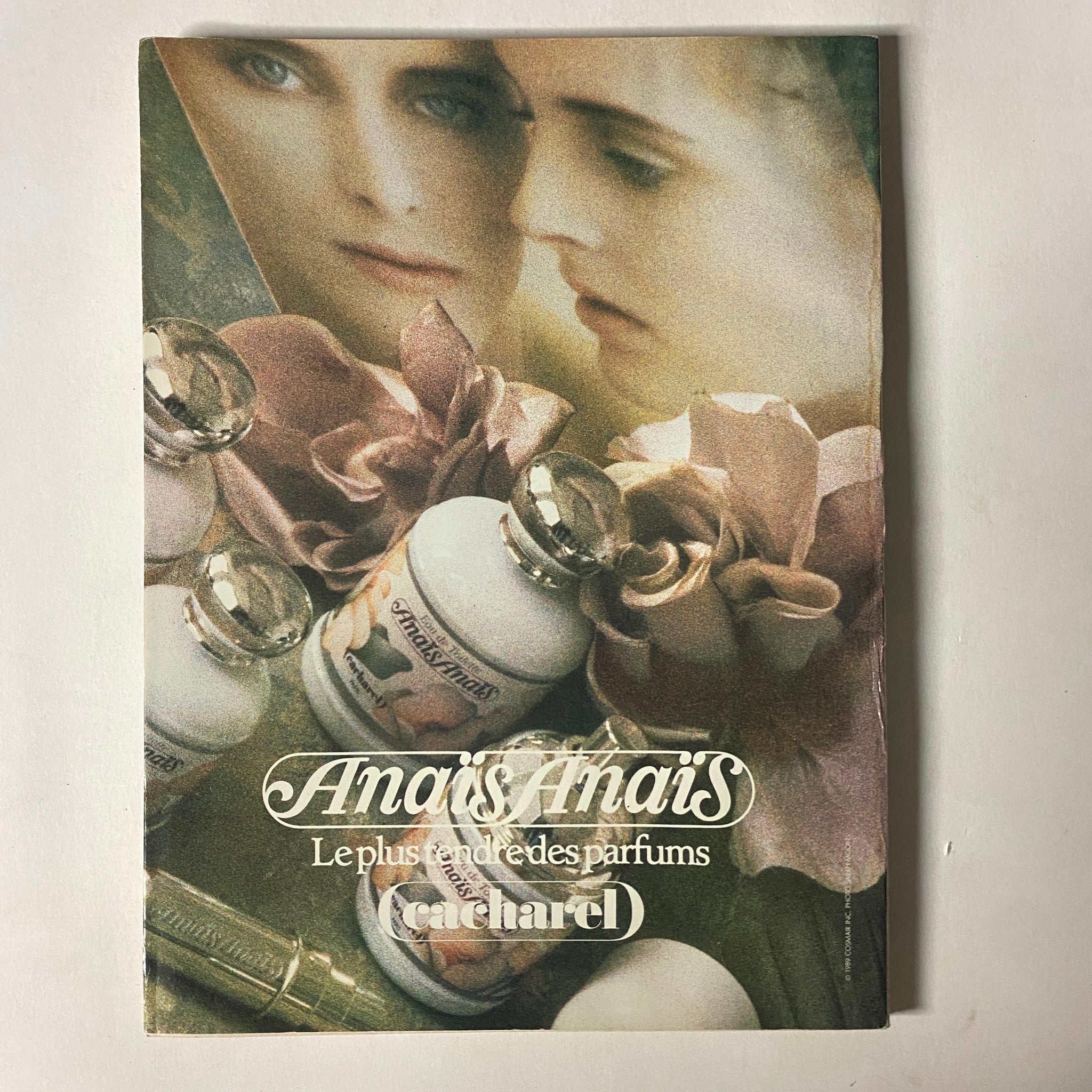 Anaïs Anaïs perfume advertisement by Cacharel, featuring elegant floral elements and two models' faces, emphasizing luxury and style in the imagery.
