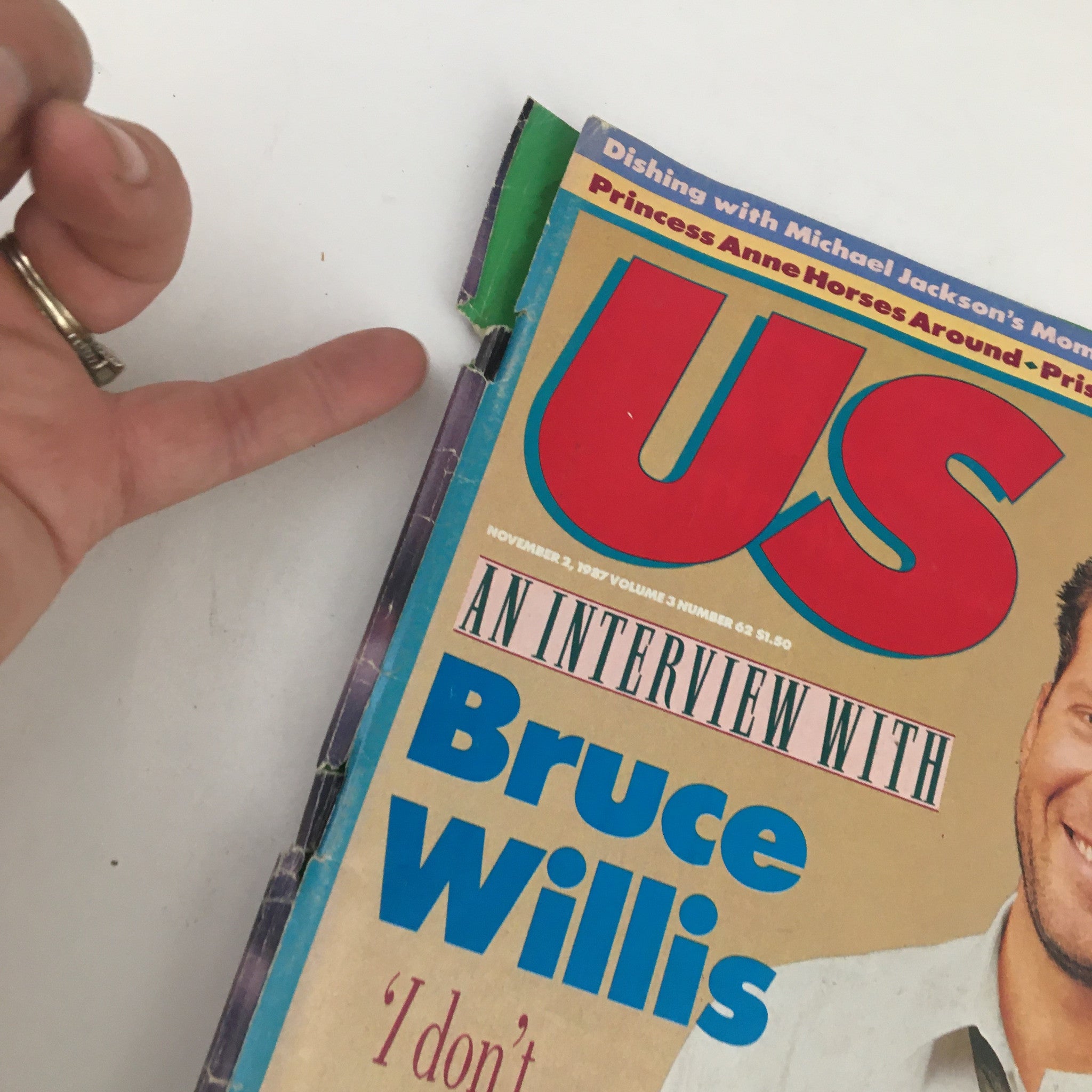 Close-up detail of the US Magazine cover dated November 2, 1987, highlighting the corner with text 'An Interview with Bruce Willis' and visible signs of age on the magazine.