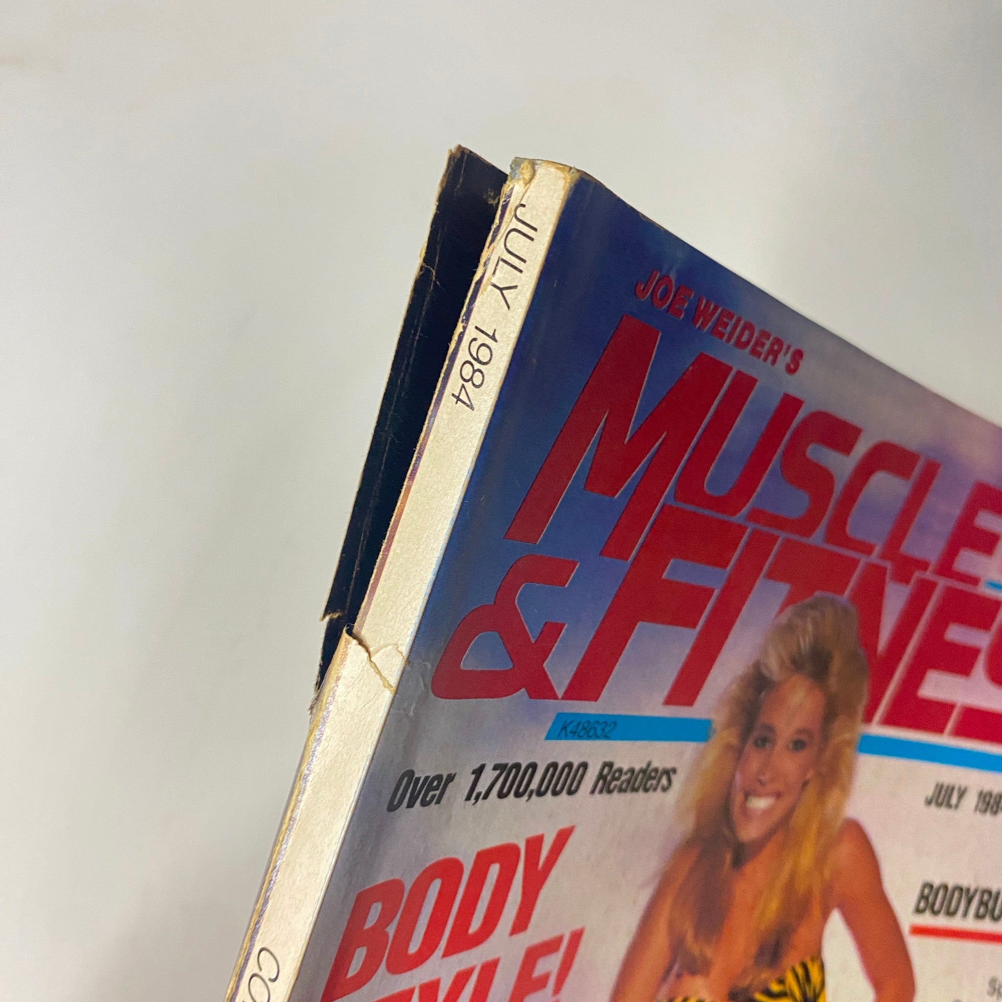 Detailed view of the top edge of the Muscle & Fitness Magazine July 1984 featuring a yellow blonde model on the cover, showcasing visible wear and tear.